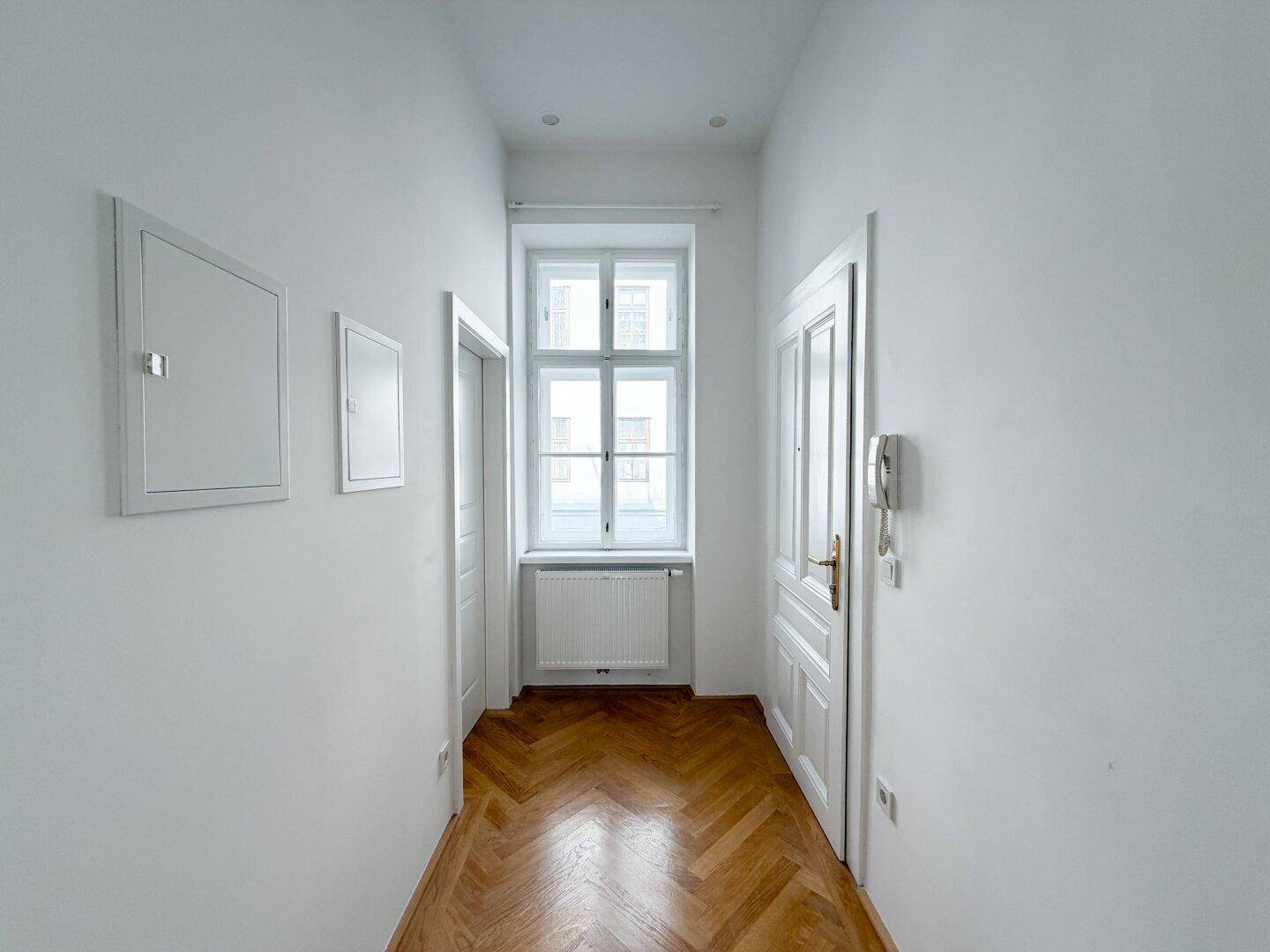 Heller Flur mit Fischgrätparkett und Fenster, der zu den verschiedenen Zimmern führt.