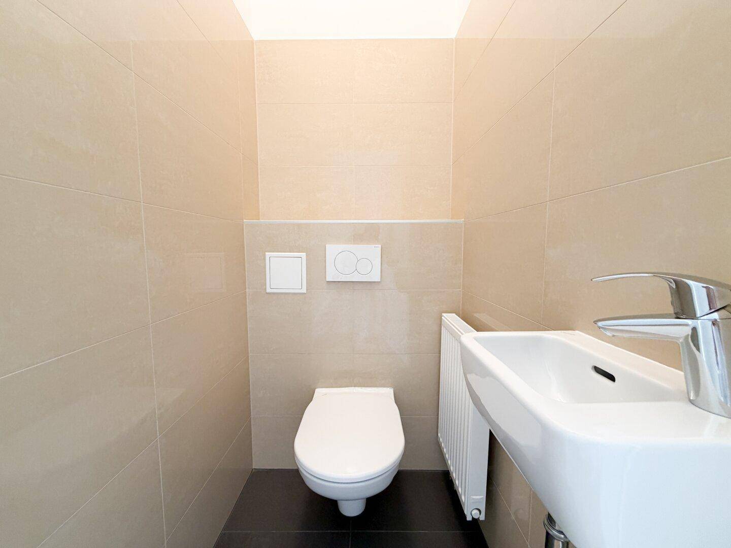 Kleines Gäste-WC mit beigen Fliesen, wandhängendem WC und kompaktem Waschbecken.