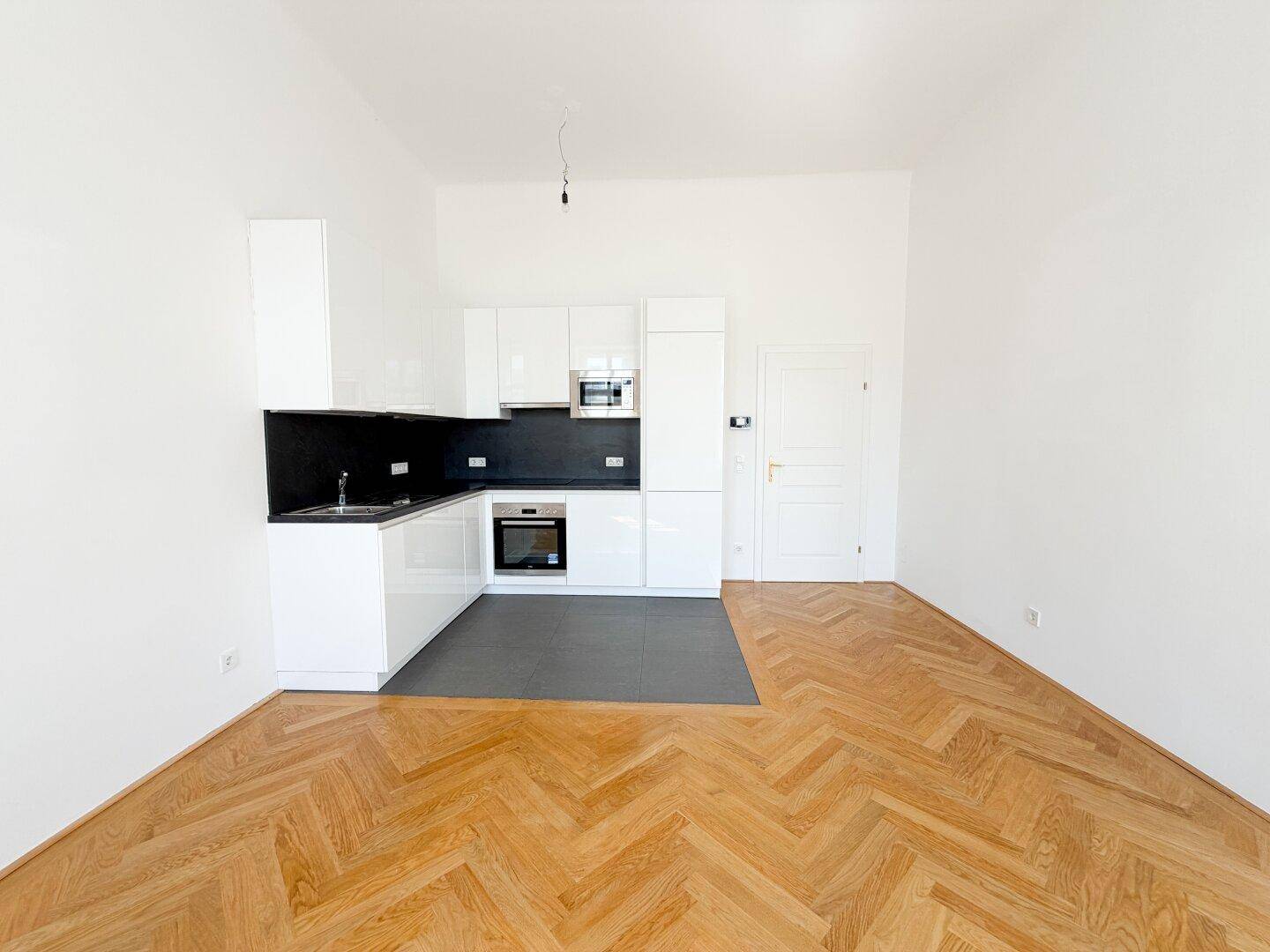 Heller Raum mit neuer, weißer Einbauküche und Fischgrätparkett, ideal für offenes Wohnen.