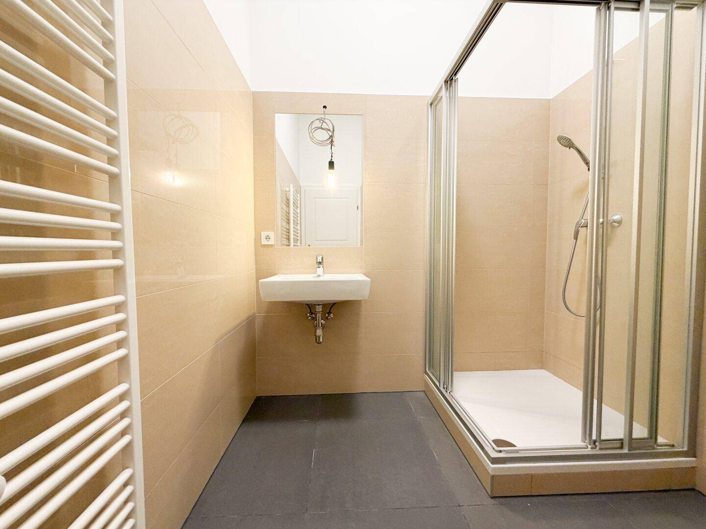 Modernes Badezimmer mit beigen Fliesen, Duschkabine, Waschbecken und beheiztem Handtuchhalter.