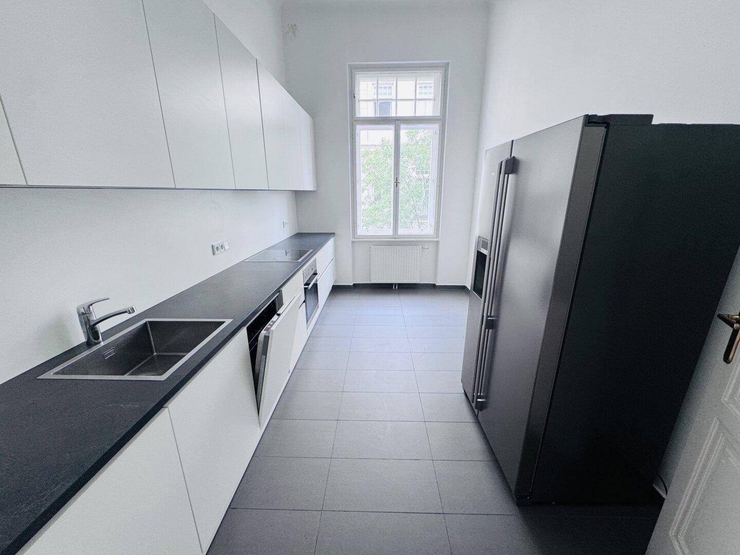 Moderne Küche mit weißen Schränken, dunklen Arbeitsplatten und einem großen Kühlschrank.