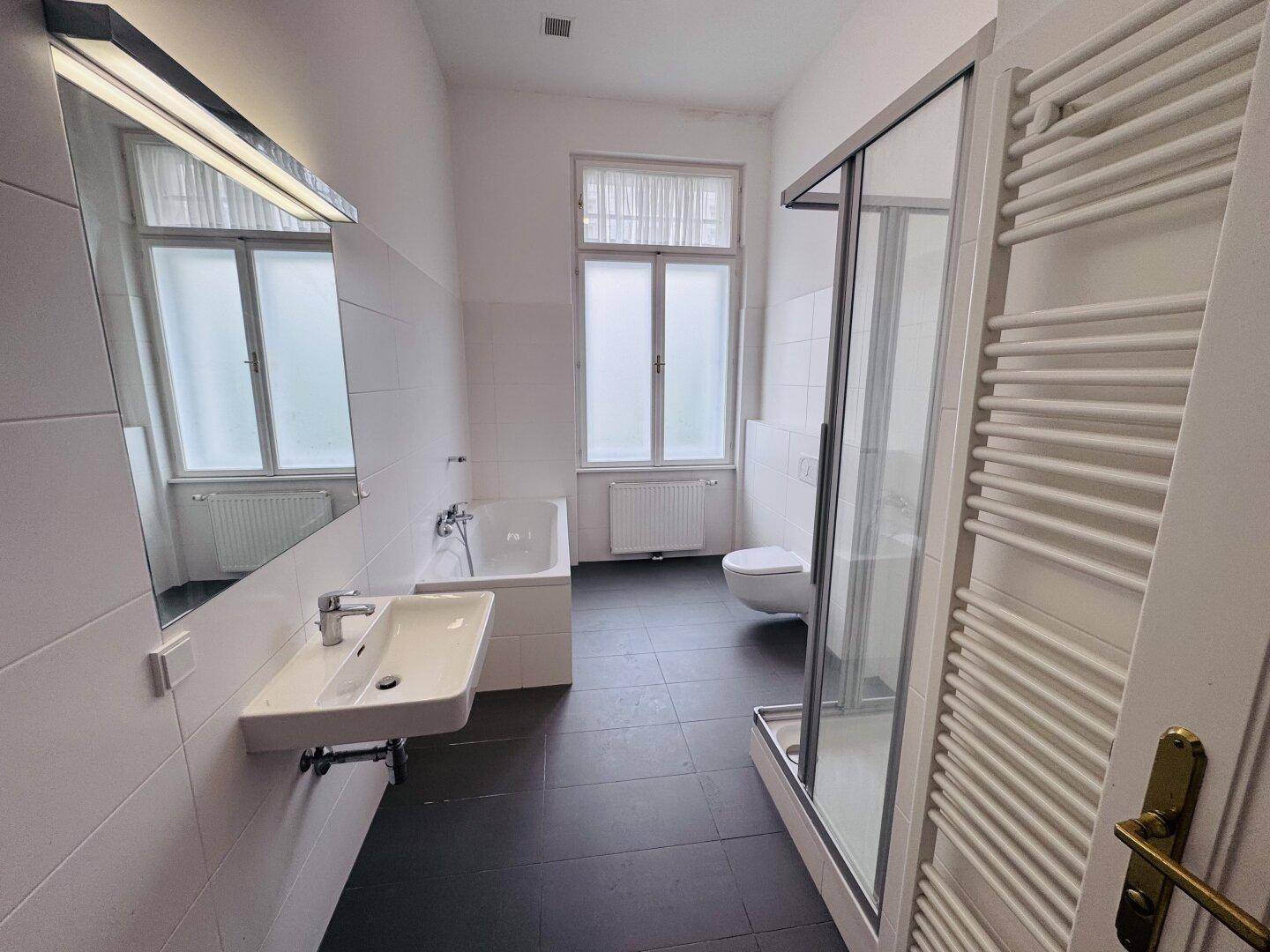 Modernes Badezimmer mit Badewanne, Duschkabine, WC und beheiztem Handtuchhalter.