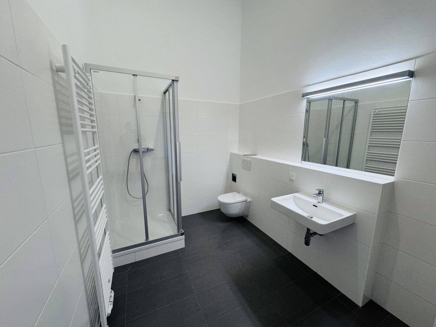 Modernes Badezimmer mit Duschkabine, WC, Waschtisch und beheiztem Handtuchhalter.