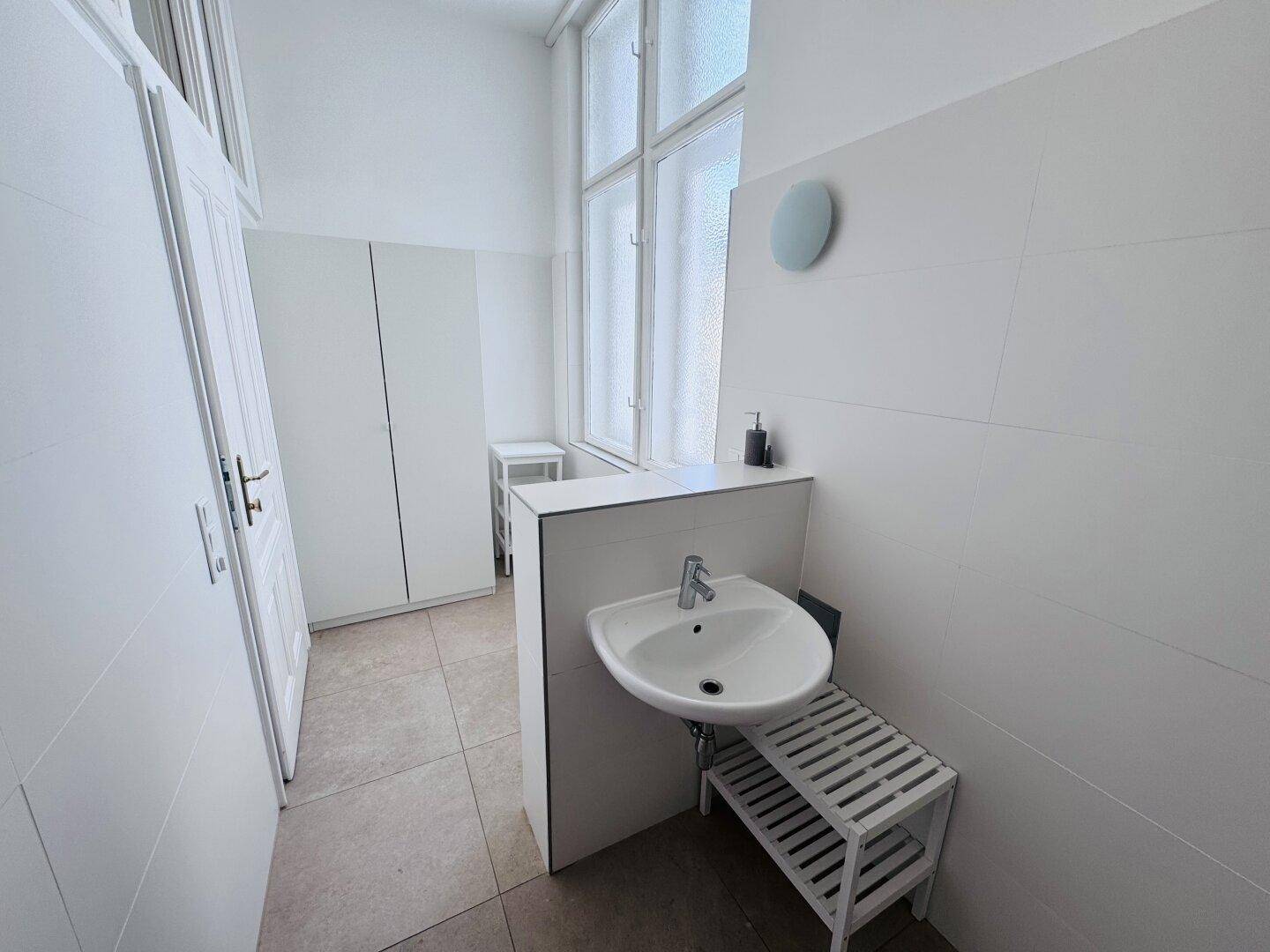 Modernes Badezimmer mit Waschbecken, weißen Wandfliesen und einem Fenster für natürliche Belüftung.