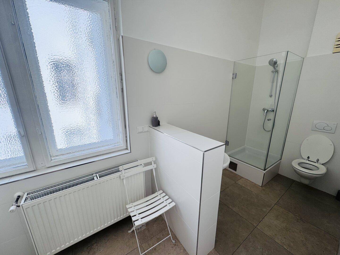Helles Badezimmer mit begehbarer Dusche, WC und Fenster, ausgestattet mit modernen Fliesen.