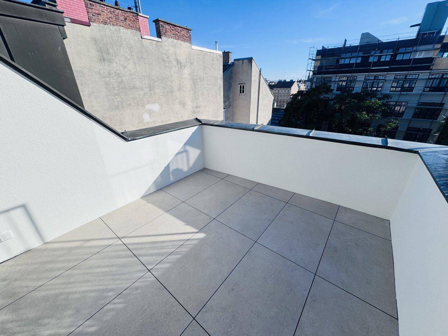 Helle Dachterrasse mit modernen grauen Fliesen und weitem Blick über die Stadt.