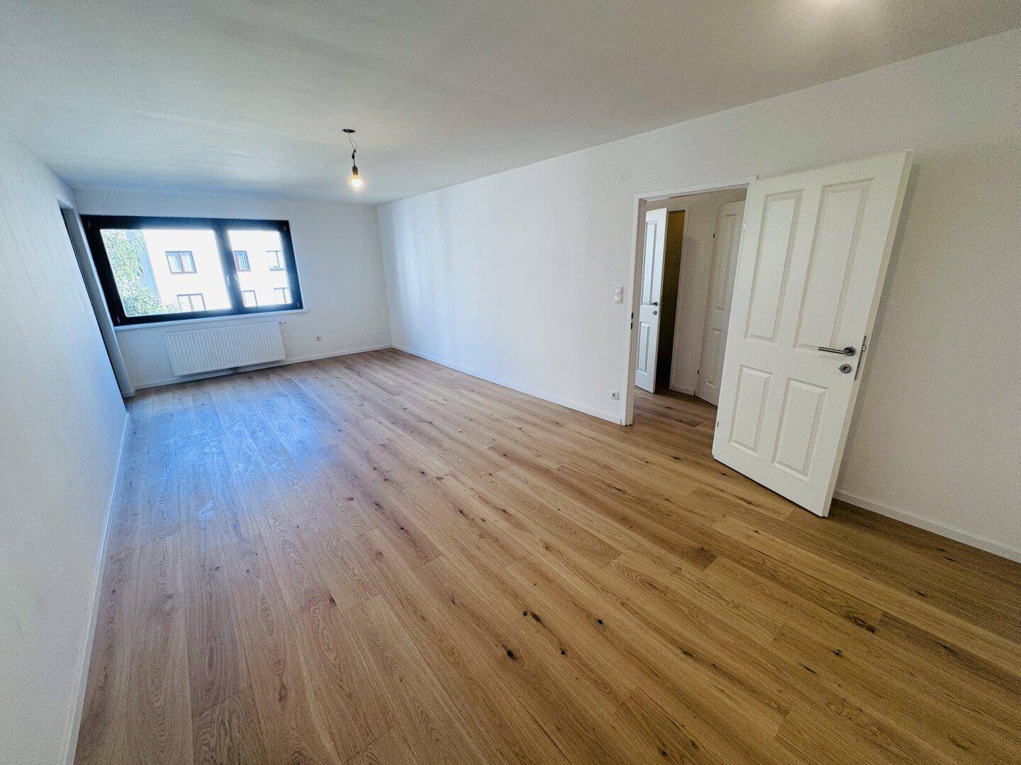 Helles, leeres Wohnzimmer mit neuem Holzdielenboden und großen Fenstern, bereit zur individuellen Gestaltung.
