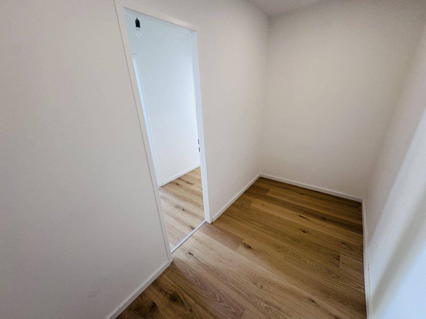 Kleiner, heller Raum mit Holzdielenboden und weißen Wänden, ideal als Abstellraum oder begehbarer Kleiderschrank.