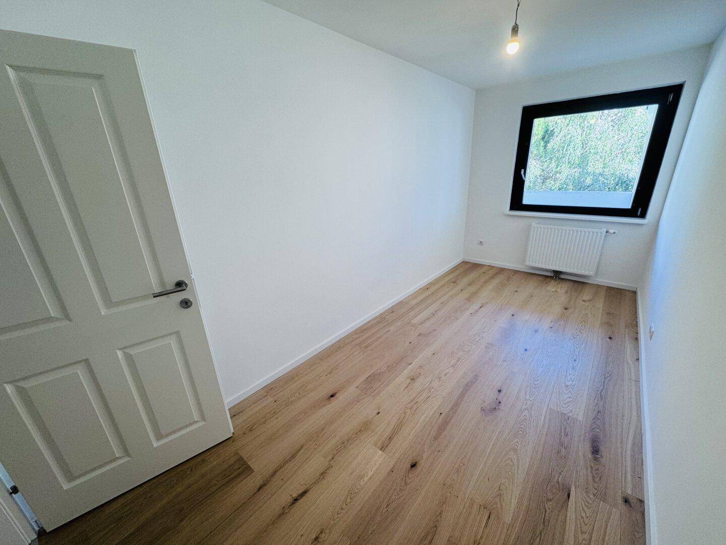 Helles Schlafzimmer mit Holzdielenboden und einem Fenster, das viel Tageslicht hereinlässt.