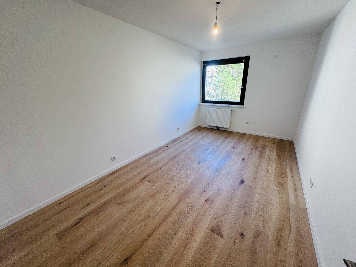 Geräumiges Schlafzimmer mit hellem Holzdielenboden und einem Fenster, das eine angenehme Atmosphäre schafft.