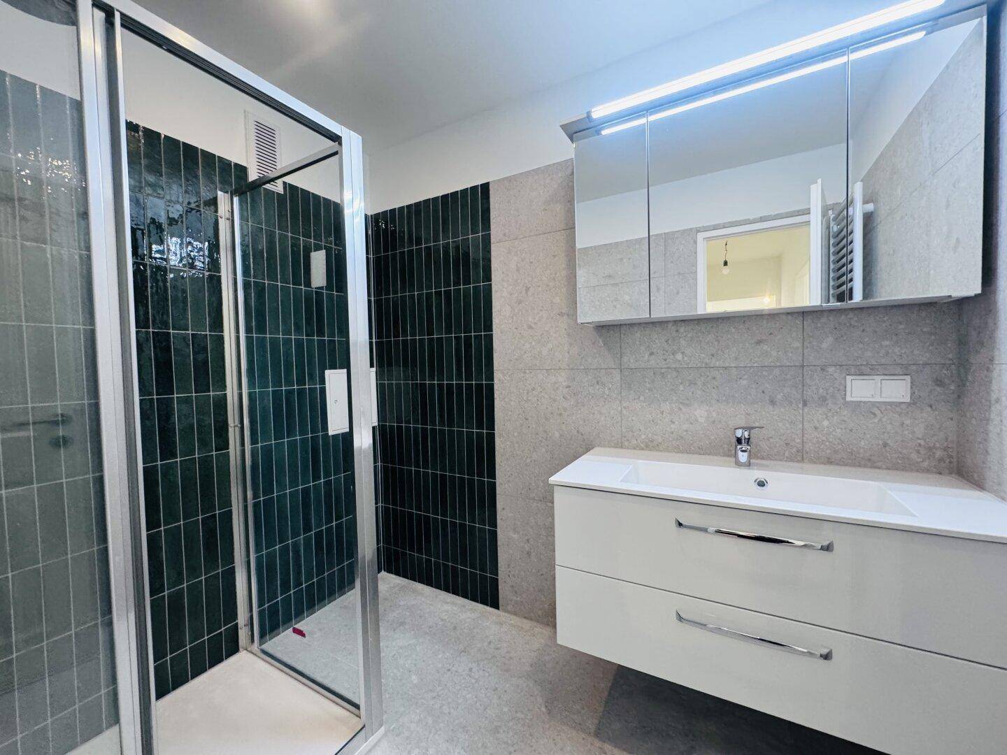 Modernes Badezimmer mit Duschkabine, Einzelwaschbecken und stilvollen grauen sowie dunkelgrünen Fliesen.