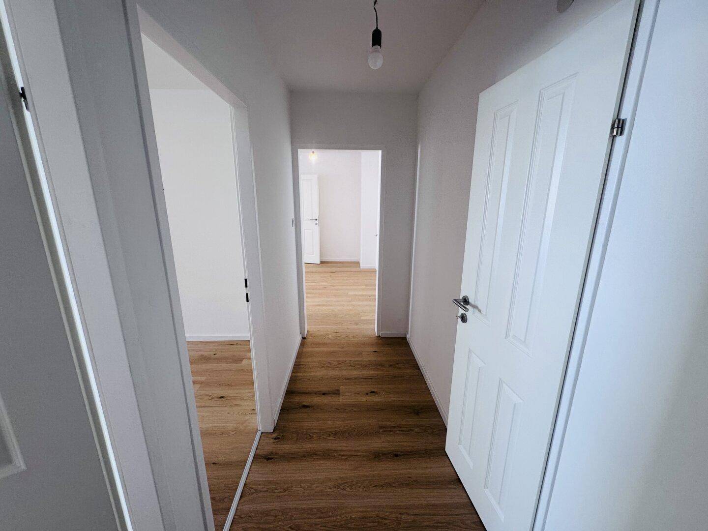 Heller Flur mit Holzdielenboden und weißen Türen, der zu verschiedenen Räumen der Wohnung führt.