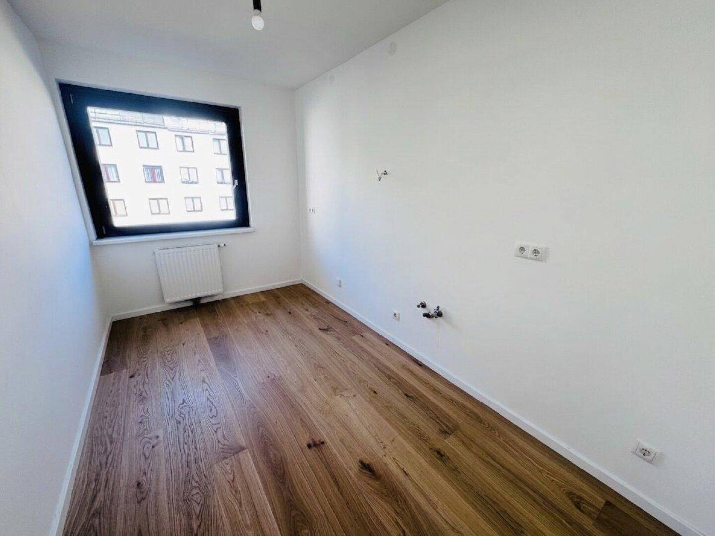Leeres Zimmer mit Holzdielenboden und Fenster, ideal als Schlafzimmer oder Arbeitszimmer, mit vorbereiteten Anschlüssen.