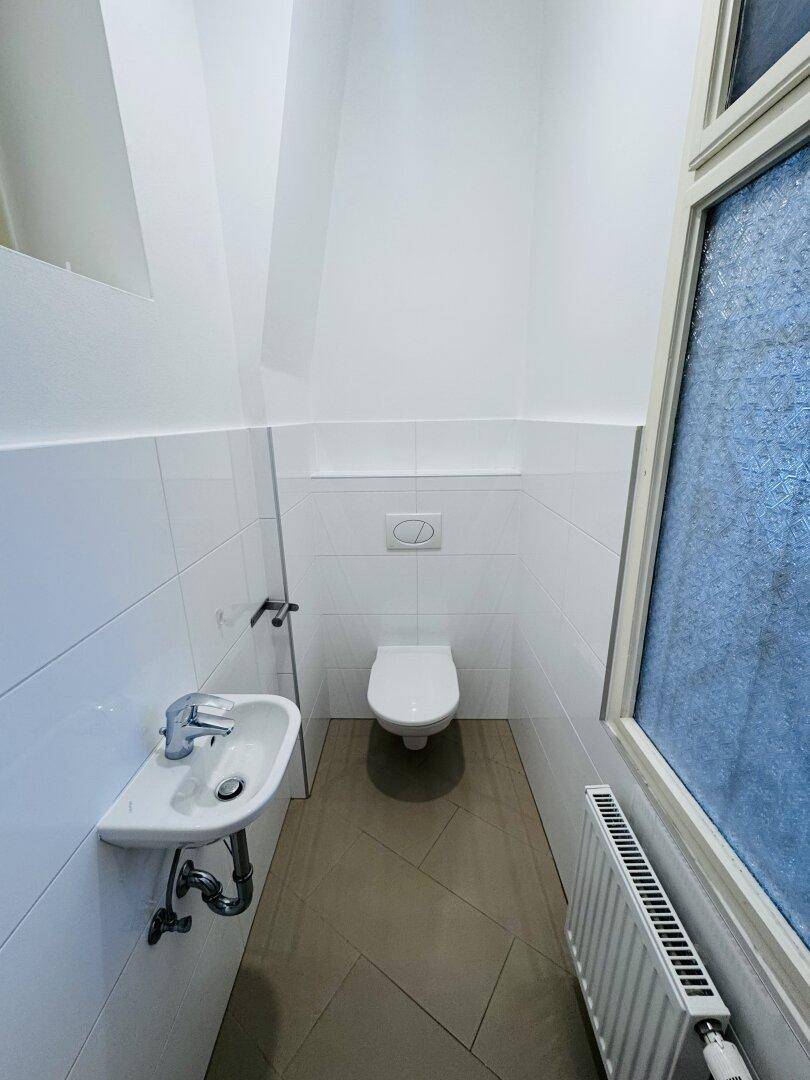 Kleines Gäste-WC mit Wand-WC, Waschbecken und einem Fenster für natürliche Belüftung.