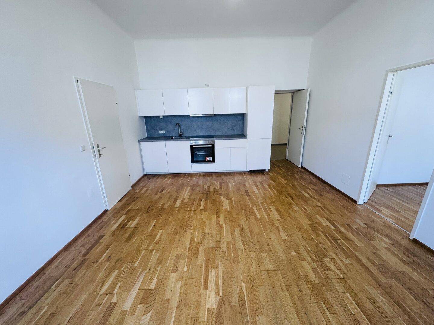 Neue, weiße Küche mit Holzparkettboden und ausreichend Platz für einen Essbereich.
