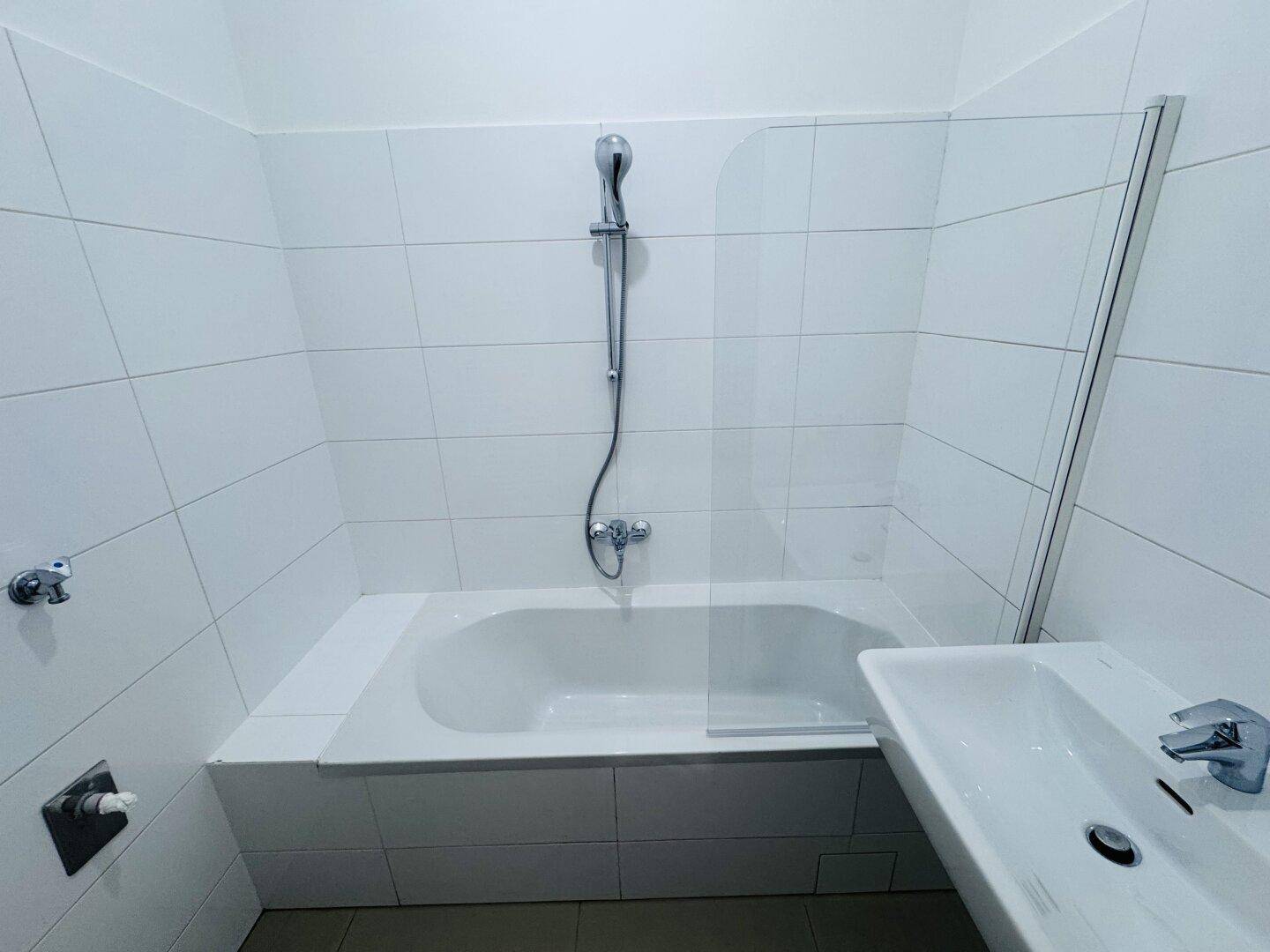 Modernes Badezimmer mit Badewanne, Duschvorrichtung und Waschbecken, komplett gefliest.
