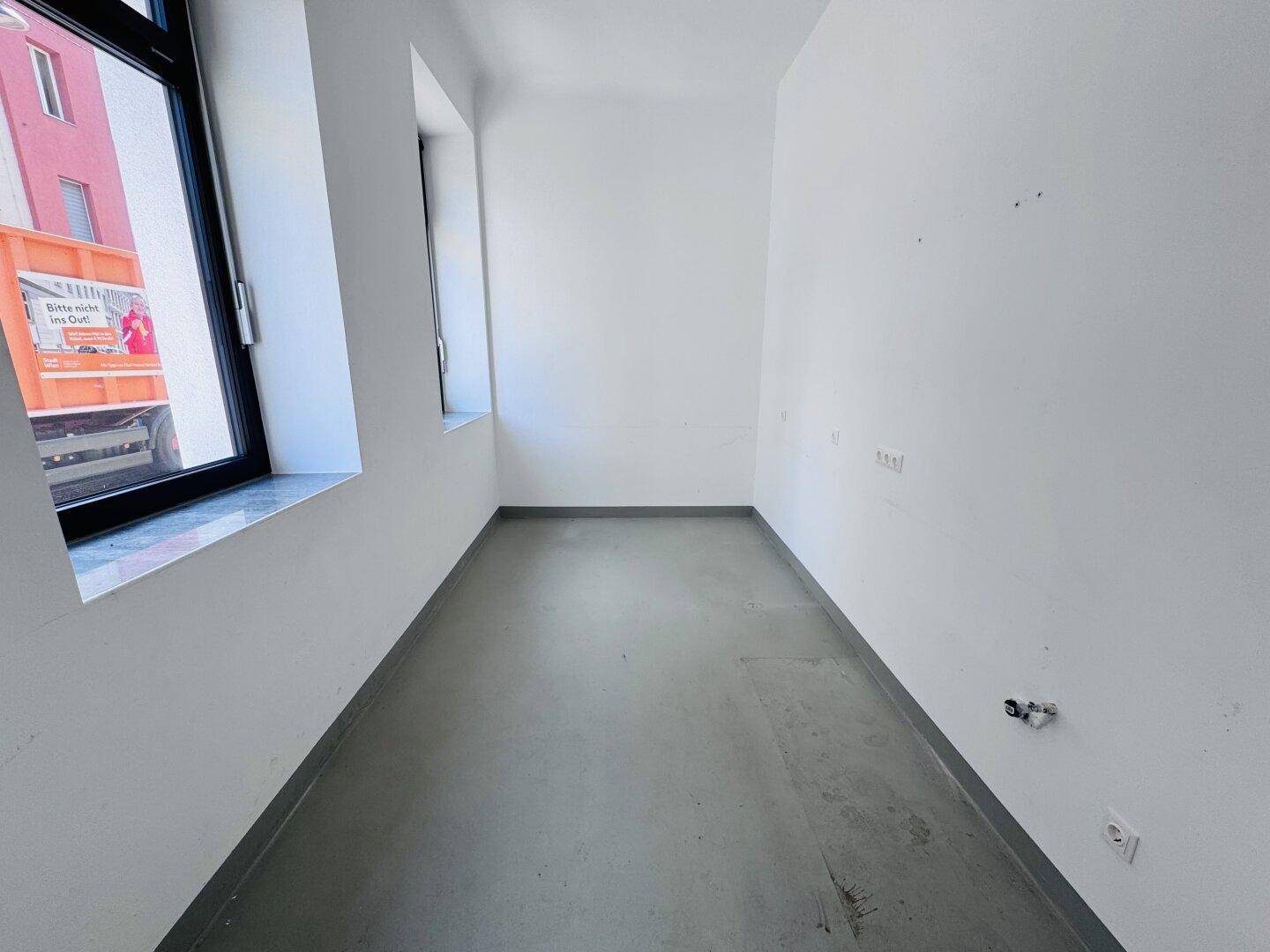 Heller, leerer Raum mit grauem Boden und zwei Fenstern, ideal als Büro.