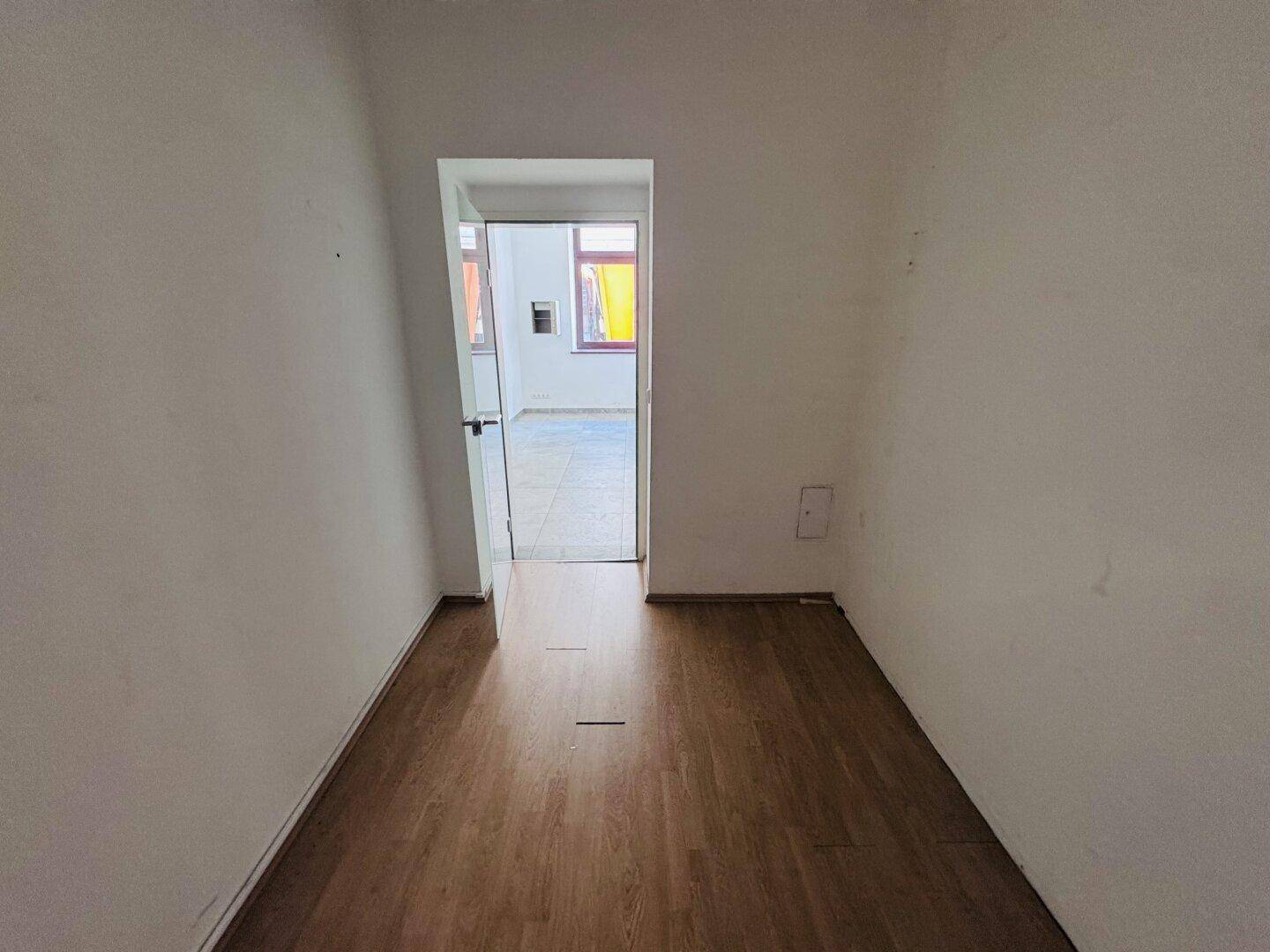 Kleiner Raum mit Holzboden und Zugang zu einem weiteren Zimmer, geeignet als Büro.