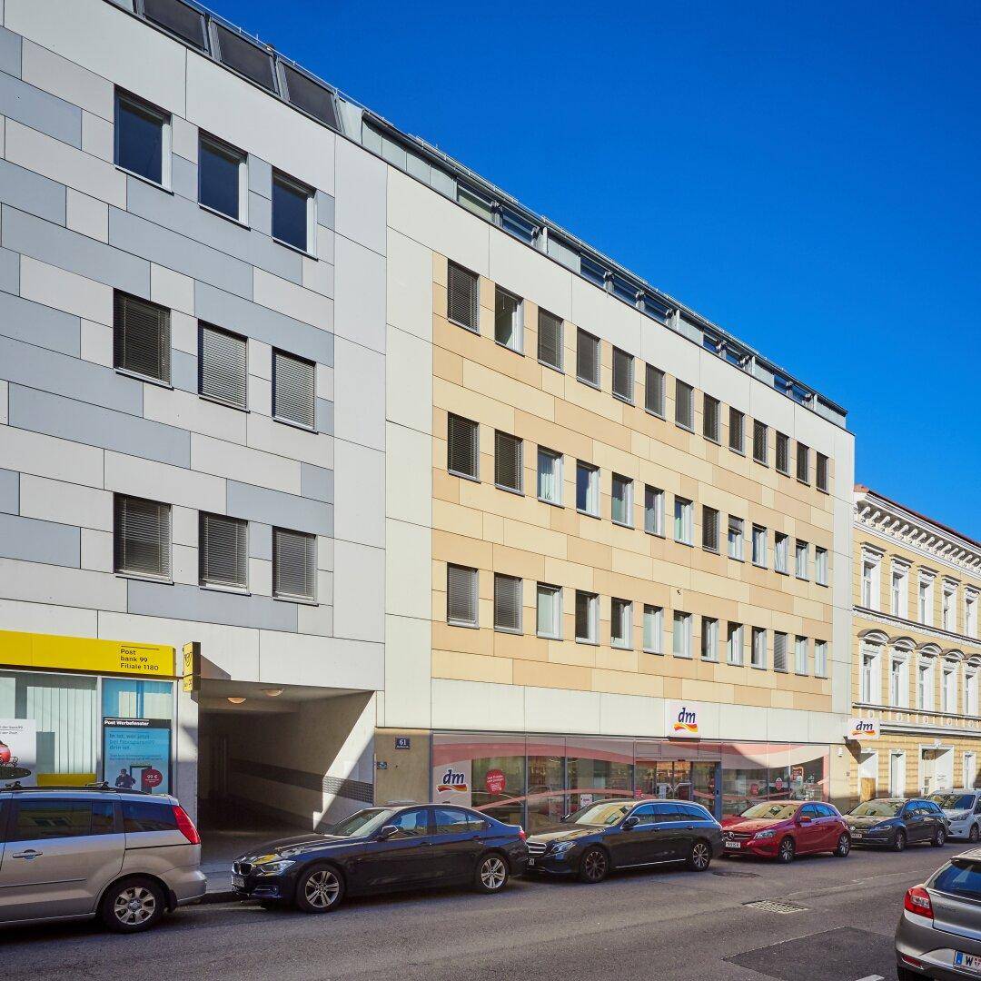 Moderne Gebäudefassade mit Geschäften im Erdgeschoss und parkenden Autos auf der Straße.