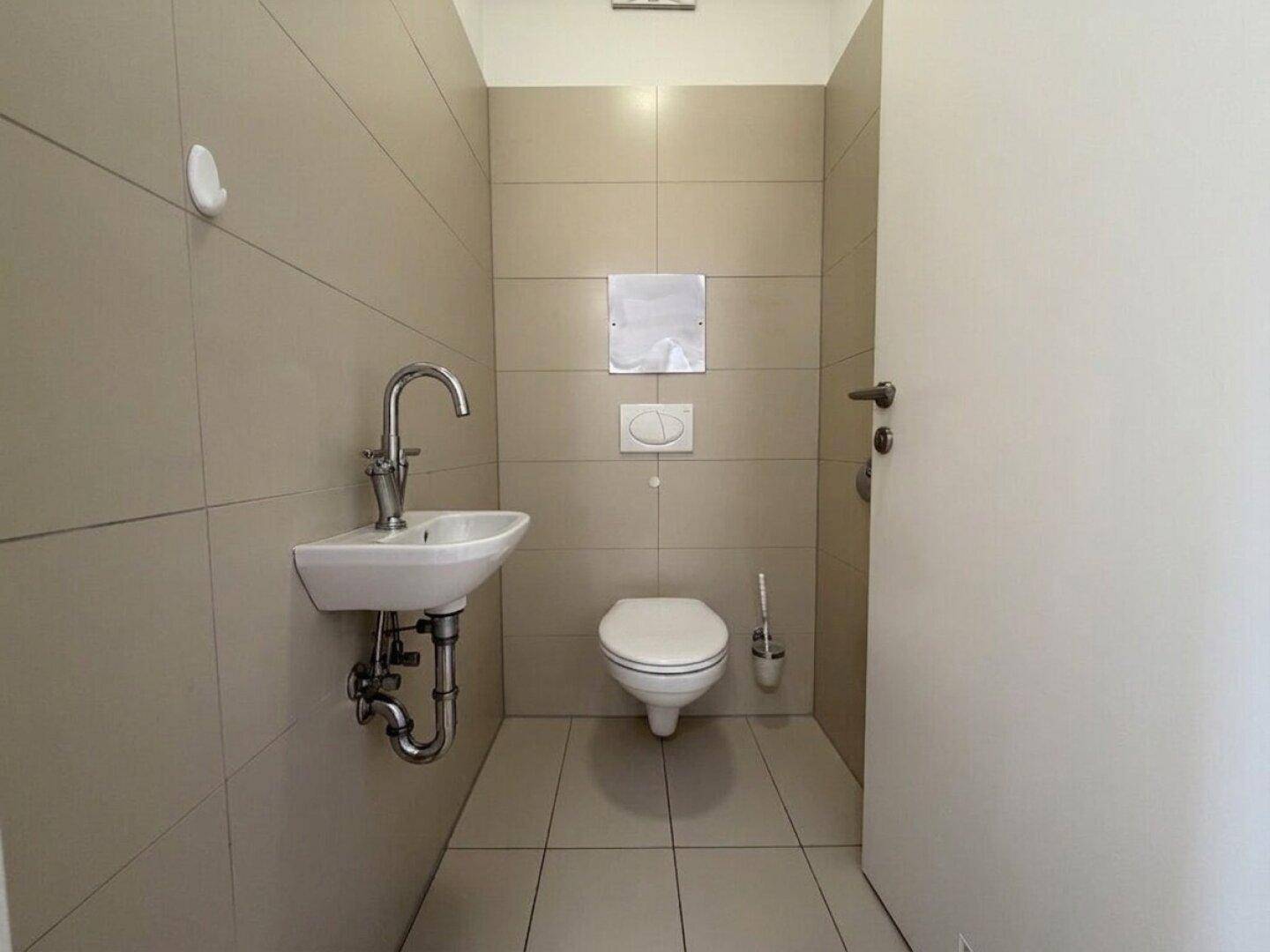 Kleines Gäste-WC mit Wand-WC, Waschbecken und hellen Fliesen an Wänden und Boden.
