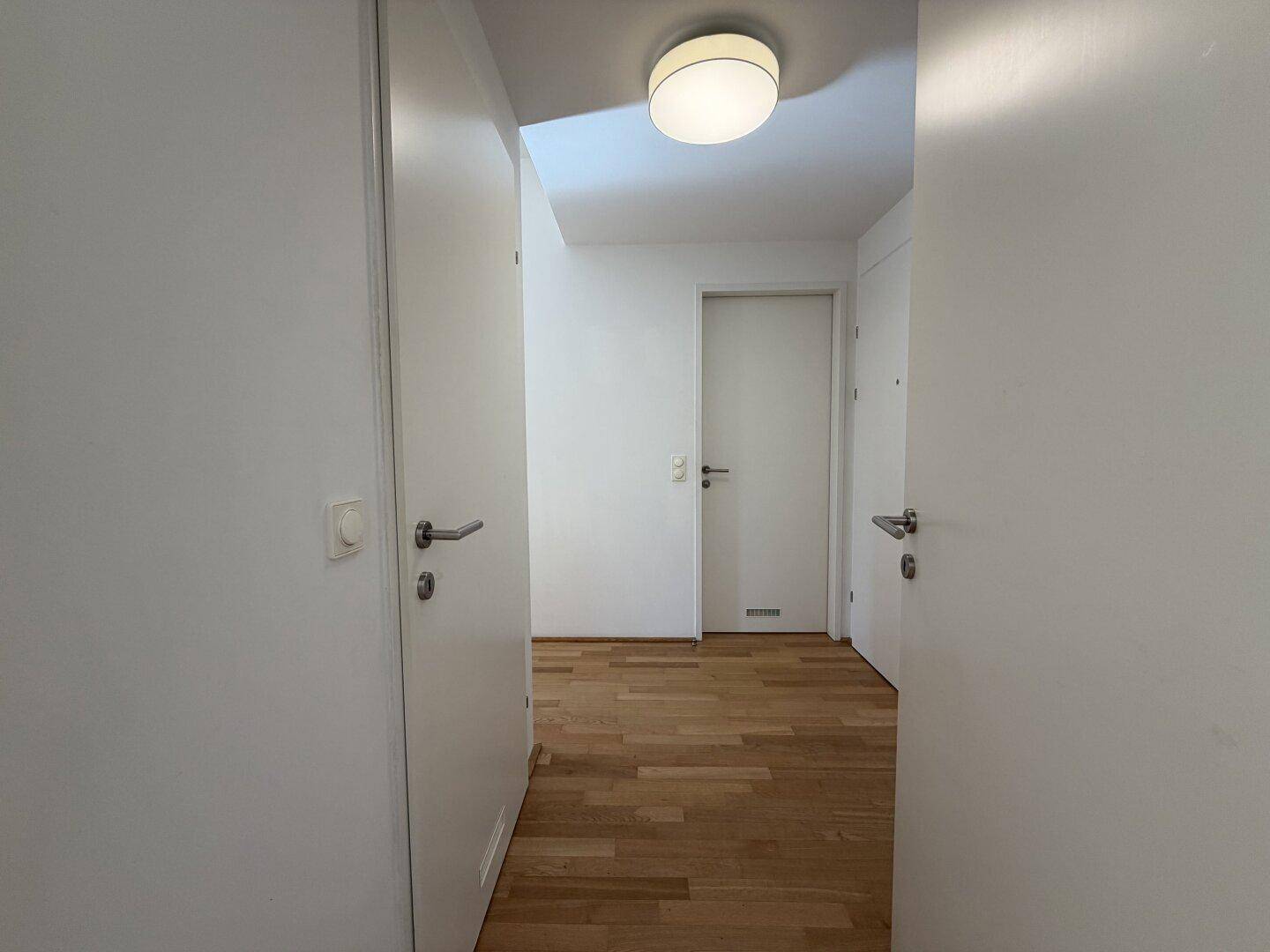 Heller Flur mit Holzboden und mehreren weißen Türen, die zu verschiedenen Räumen führen.