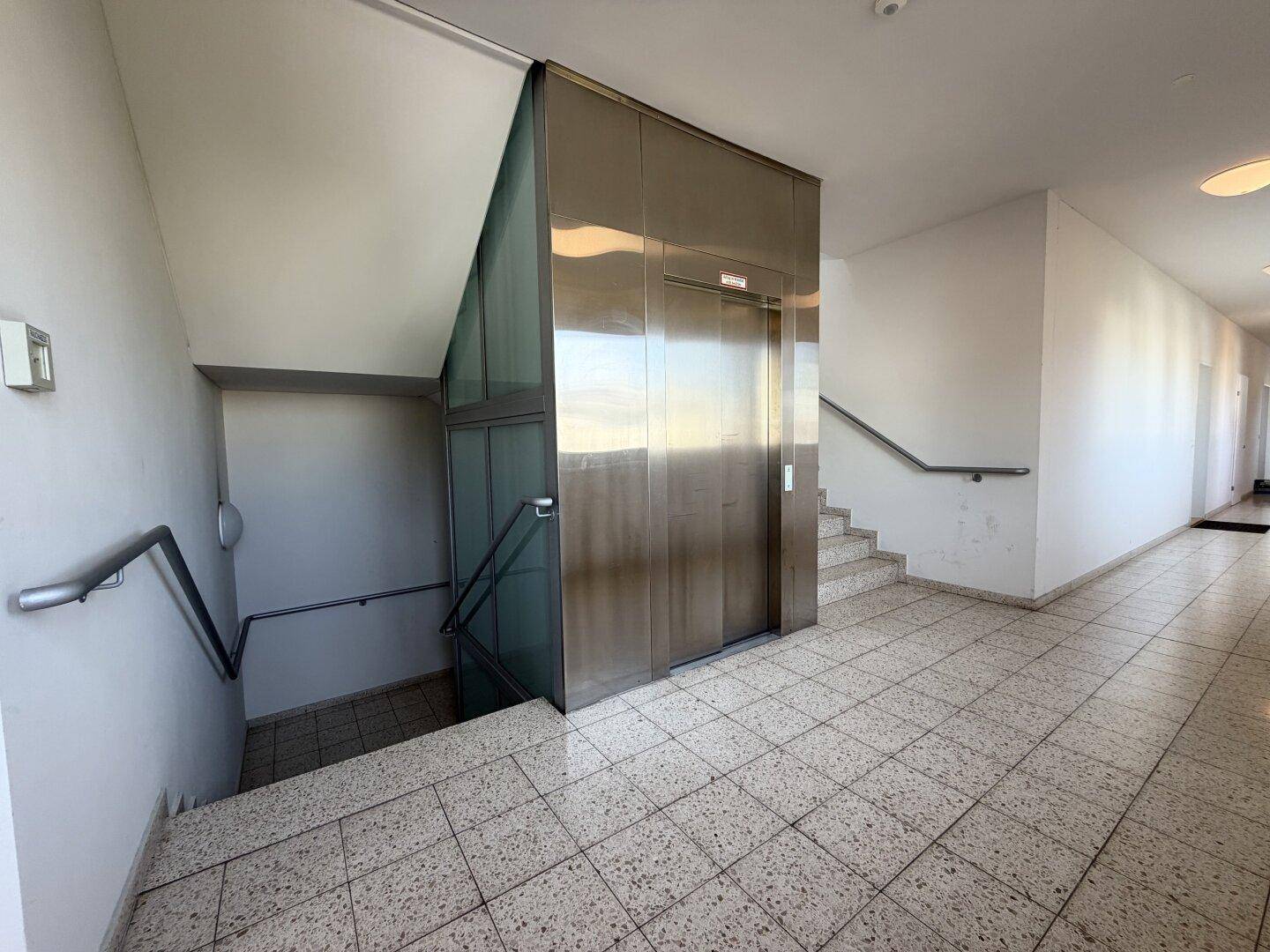 Heller Eingangsbereich mit Treppenhaus und modernem Aufzug, ausgestattet mit Fliesenboden.