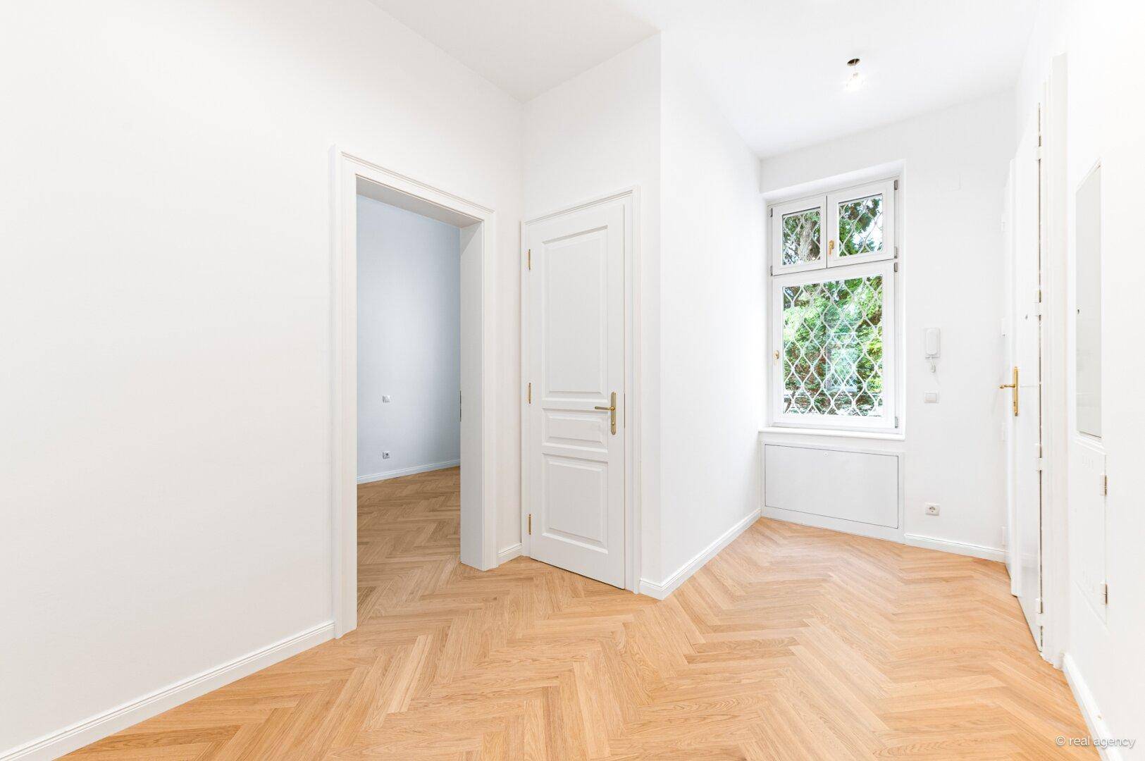 Heller Flur mit Fischgrätparkett und Fenster, der zu weiteren Räumen führt.