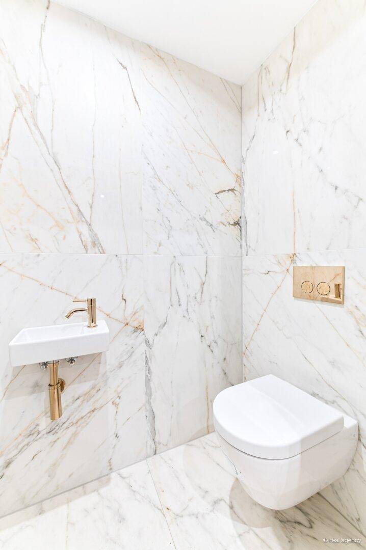 Modernes Gäste-WC mit Marmorfliesen, wandhängender Toilette und kleinem Waschbecken.