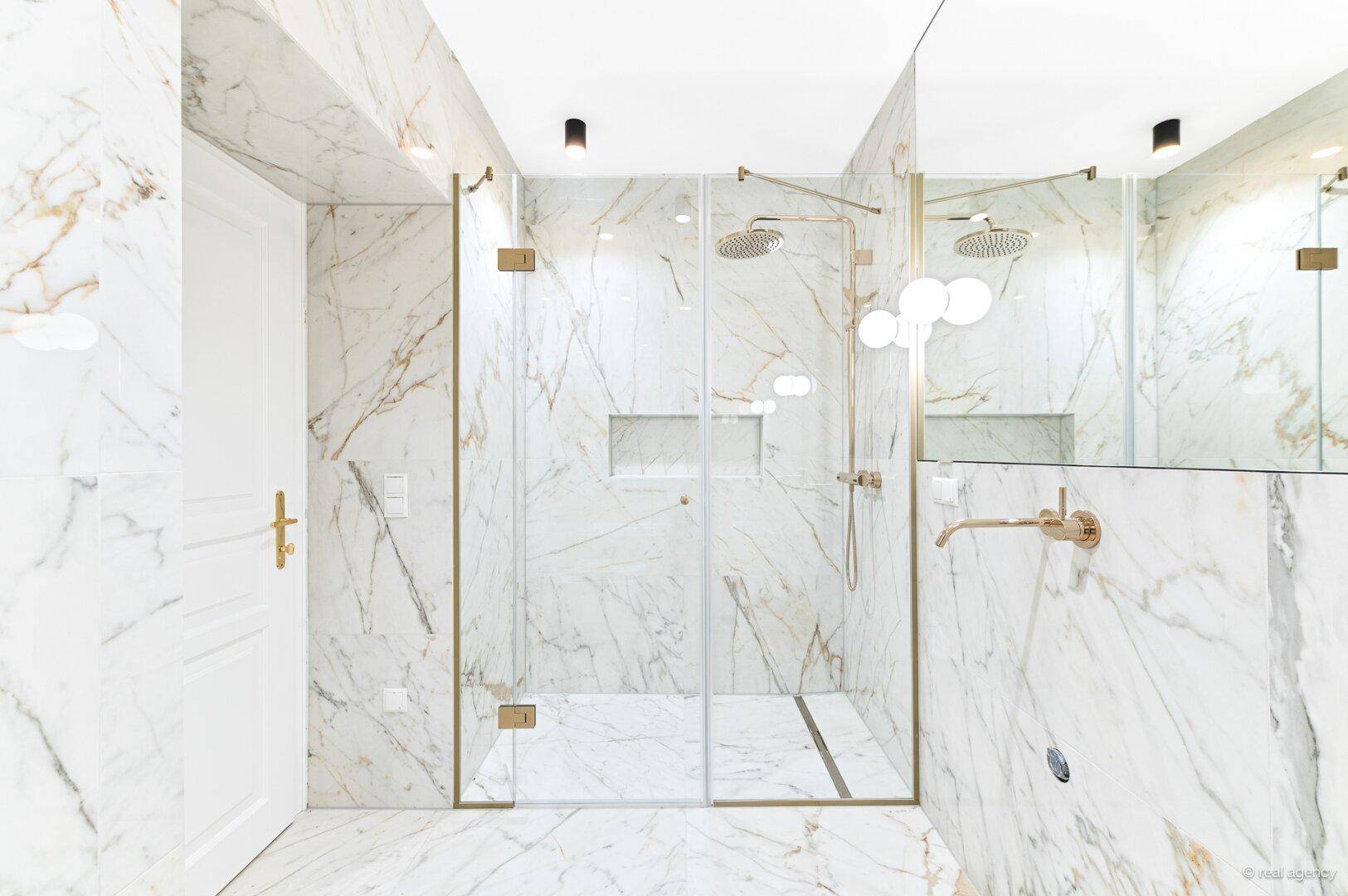 Luxuriöses Badezimmer mit Marmorfliesen, begehbarer Dusche und eleganten goldenen Armaturen.
