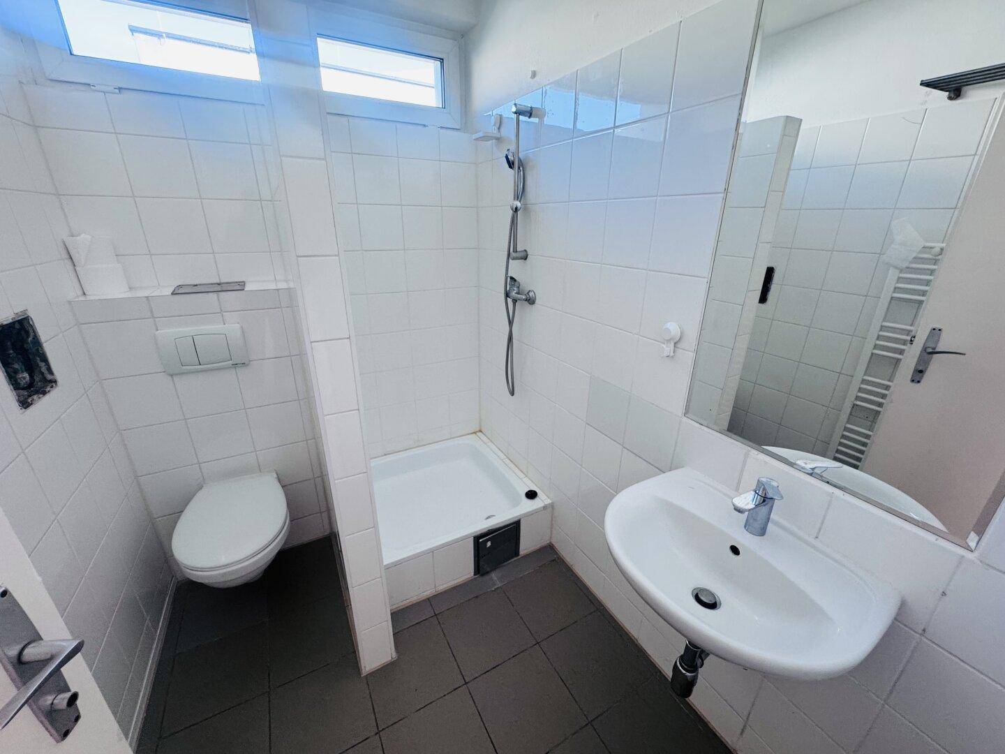 Funktionales Badezimmer mit Dusche, WC, Waschbecken und weißen Fliesen an den Wänden.