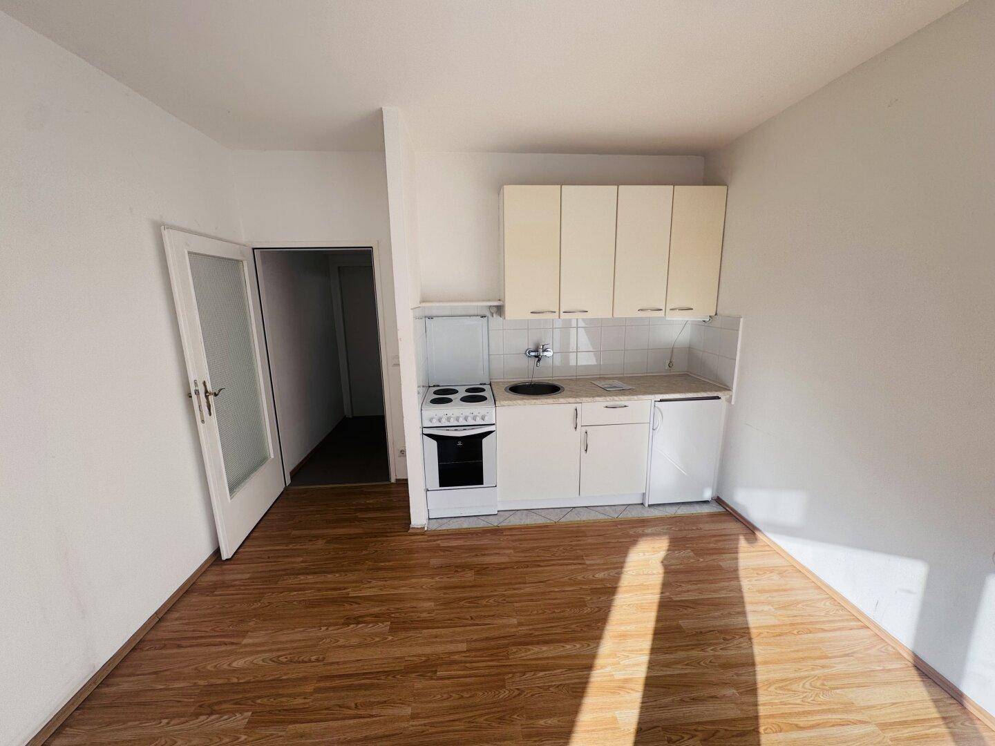 Gemütlicher Wohnbereich mit integrierter Kochnische und hellem Laminatboden.