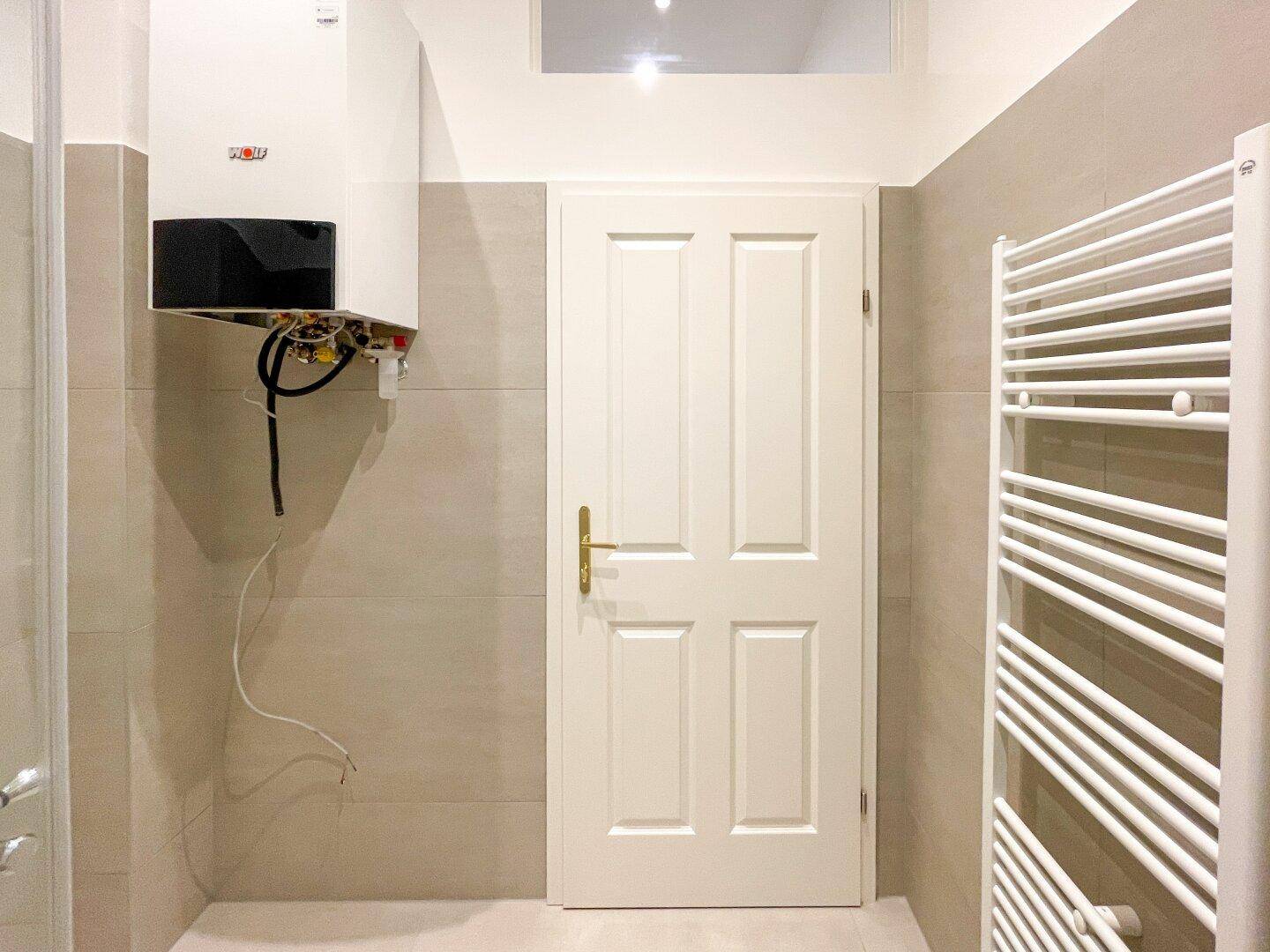 Funktionales Badezimmer mit Gastherme, weißer Tür und praktischem Handtuchheizkörper.