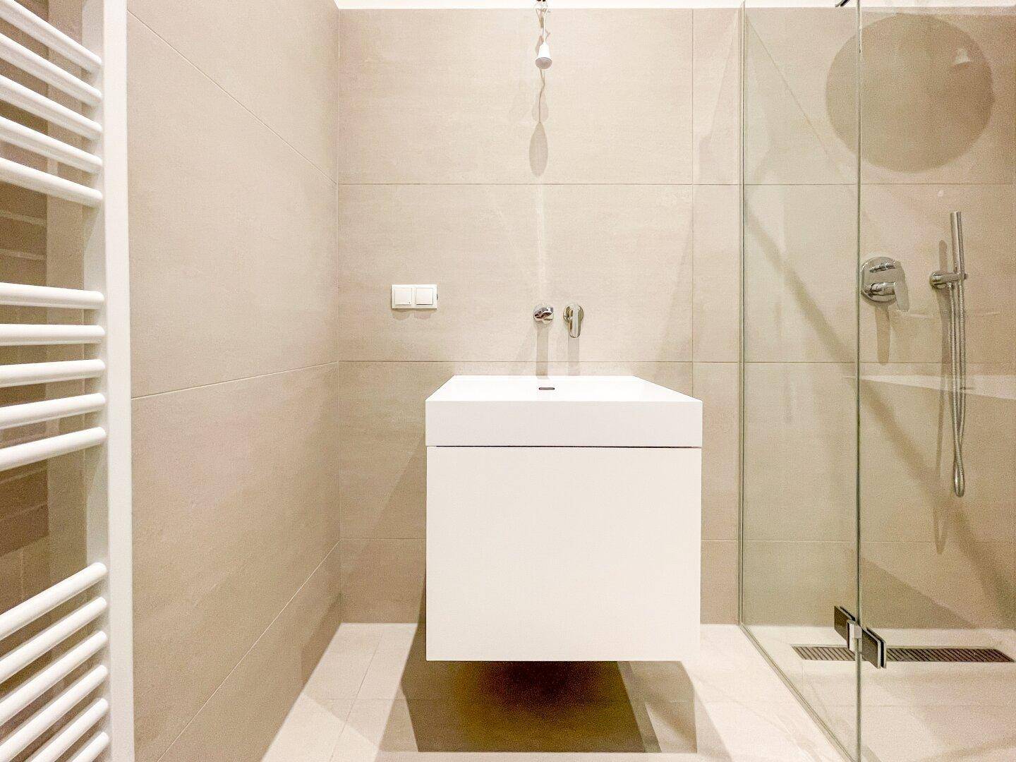 Modernes Badezimmer mit schwebendem Waschtisch, großer Duschkabine und beheiztem Handtuchhalter.