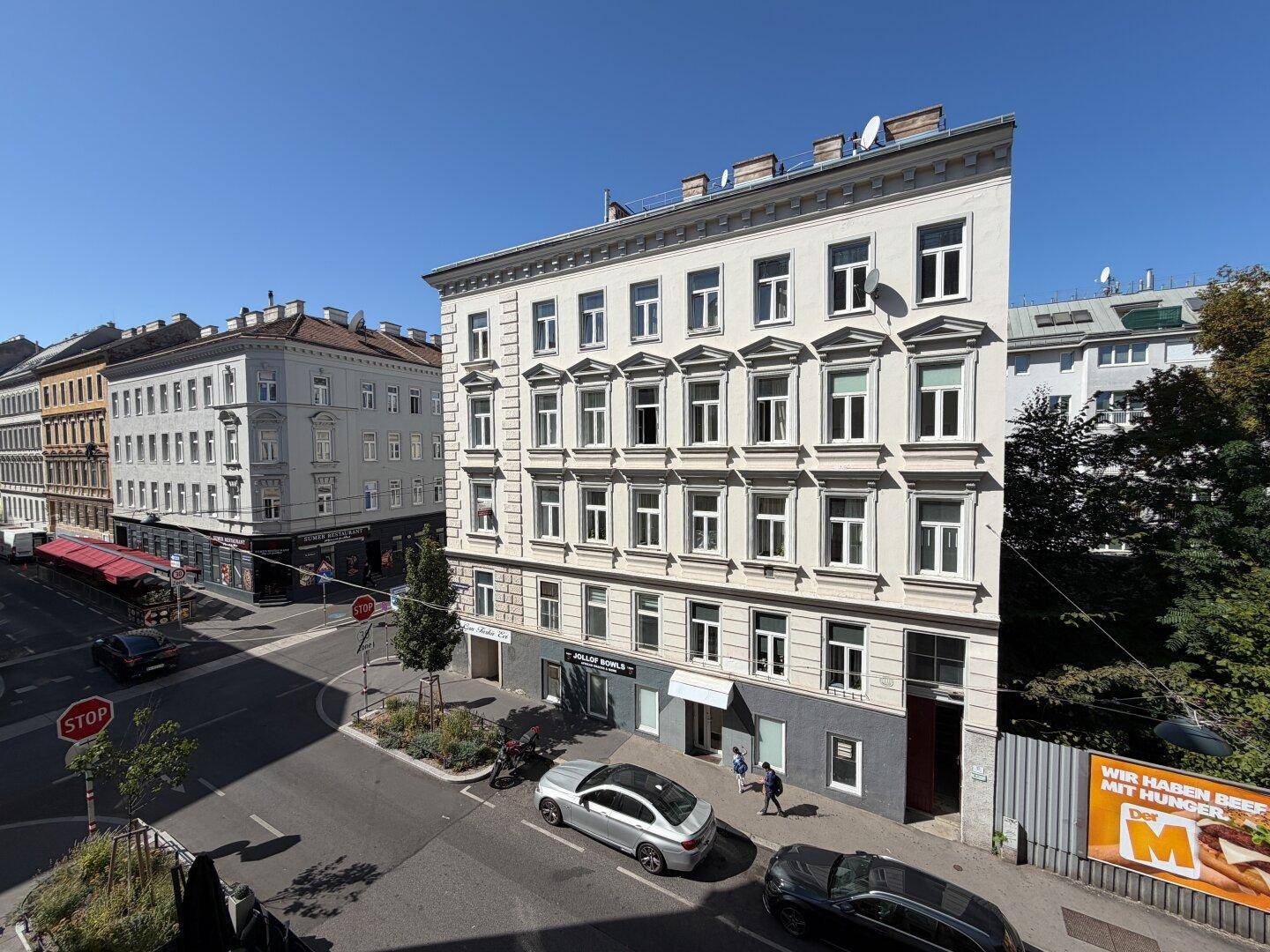 Panoramablick auf ein Eckgebäude in der Stadt mit belebter Straße und klarem Himmel.