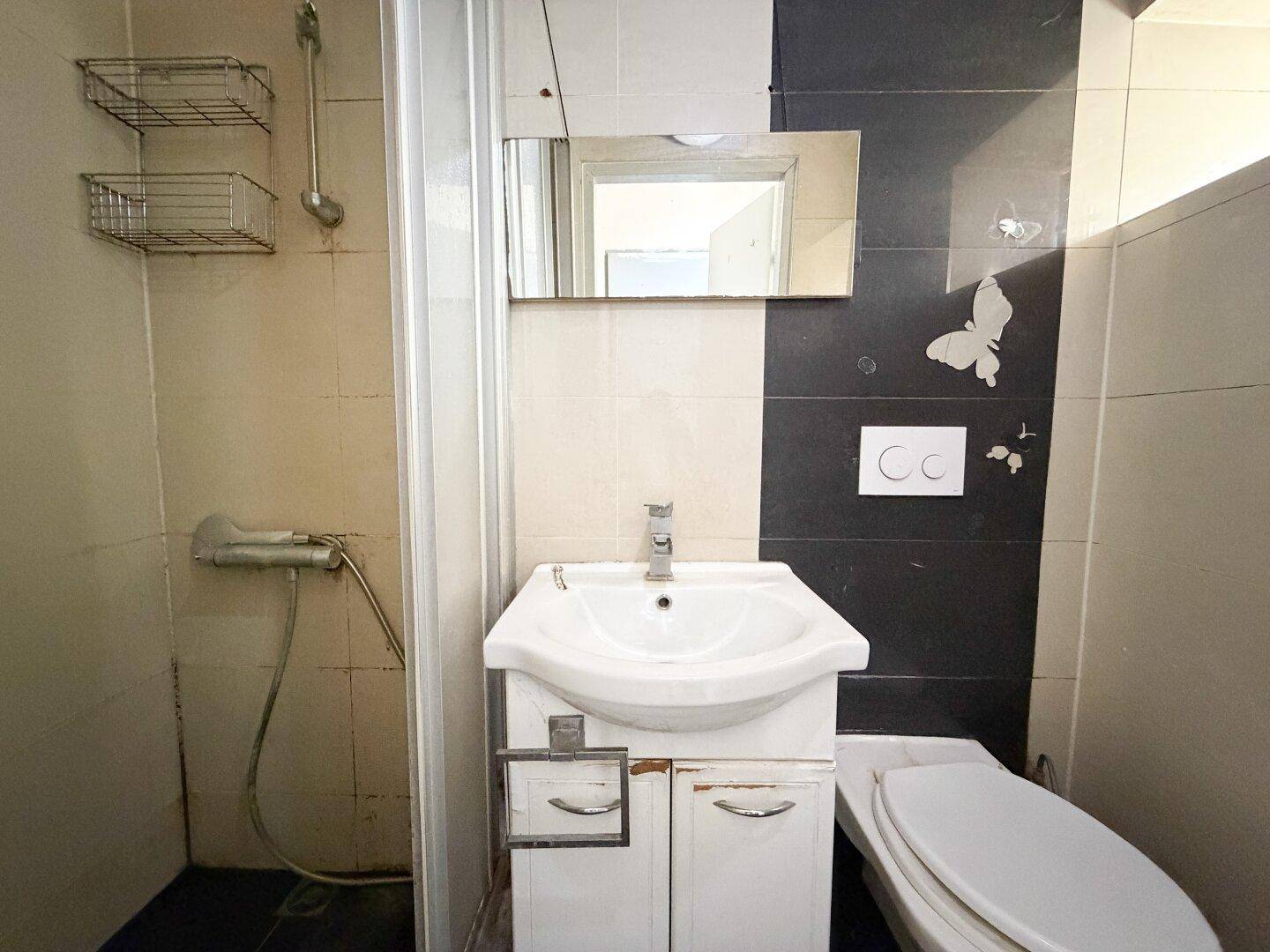 Kleines Badezimmer mit Dusche, Waschbecken und Toilette, gefliest in Schwarz und Beige.