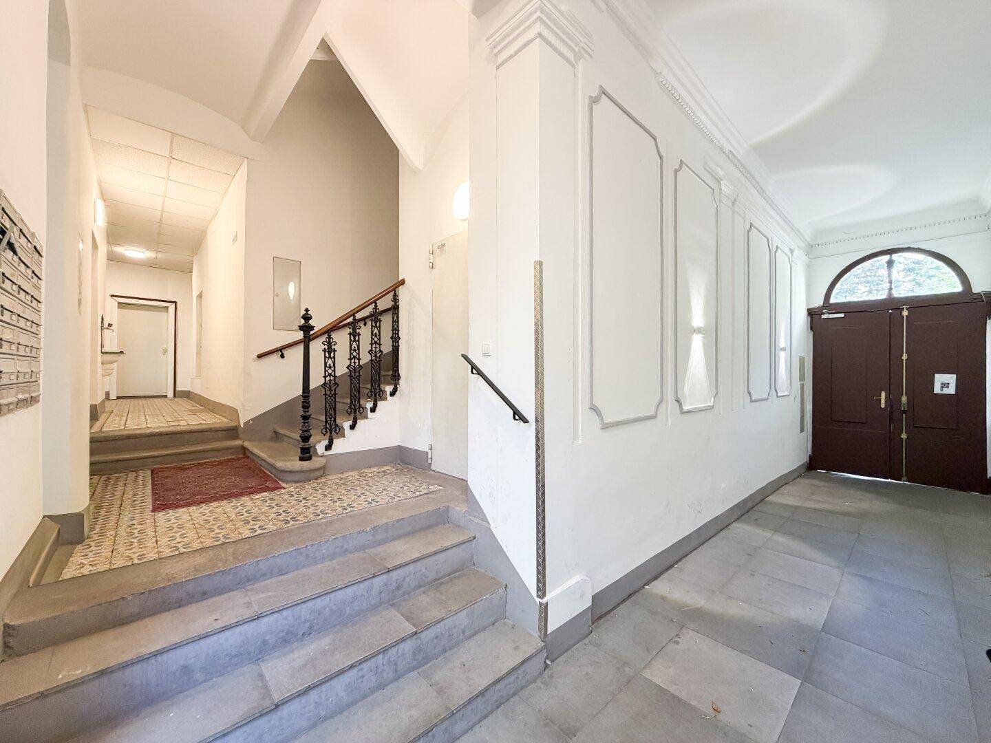 Repräsentativer Eingangsbereich eines Altbaus mit historischer Treppe und gemusterten Fliesen.