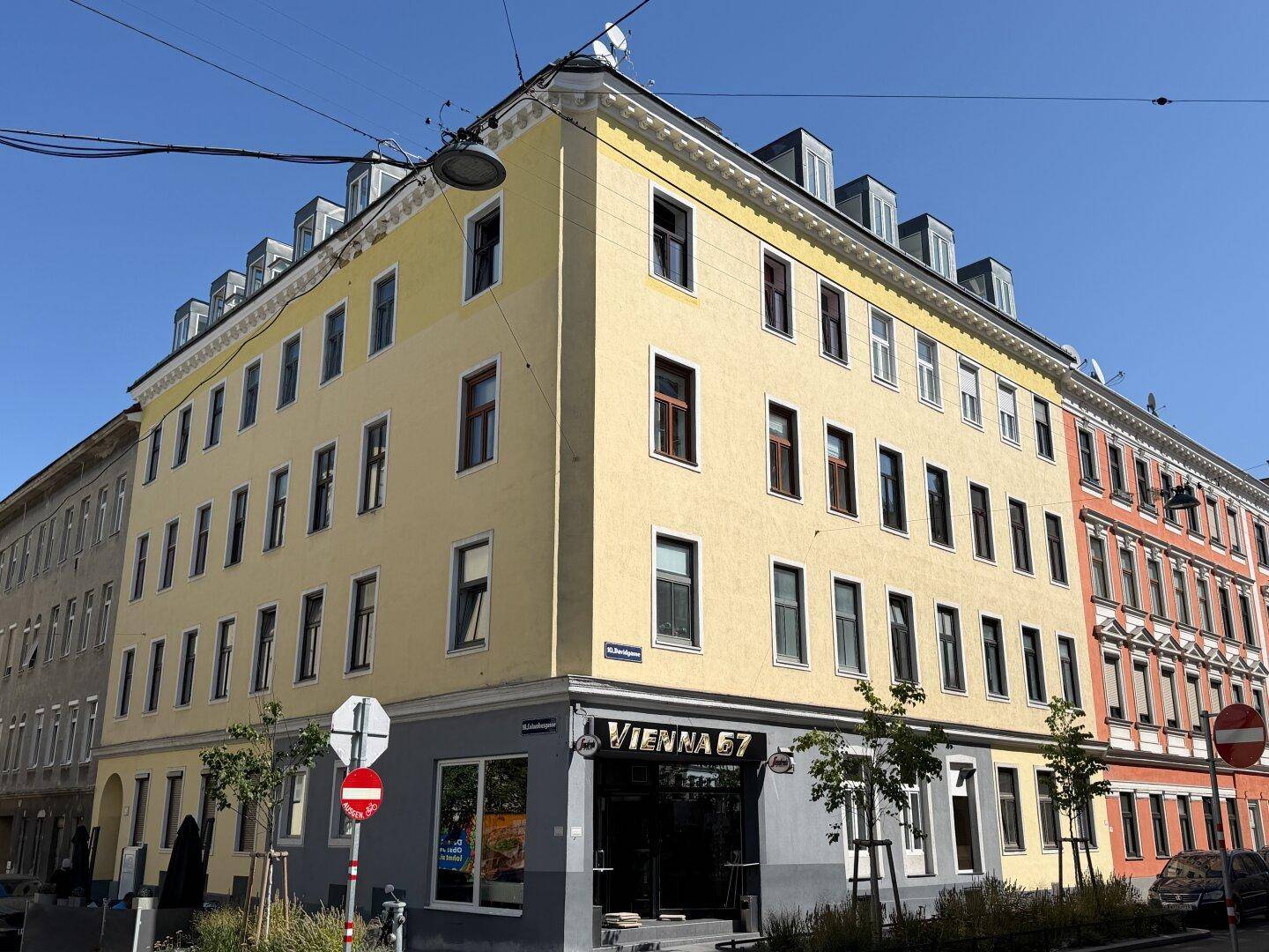 Eckgebäude mit gelber Fassade und Geschäften im Erdgeschoss an einer städtischen Straße.