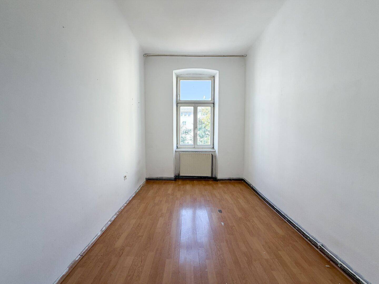 Schmaler Raum mit Holzboden, einem Fenster und Heizkörper, ideal als Schlaf- oder Arbeitszimmer.