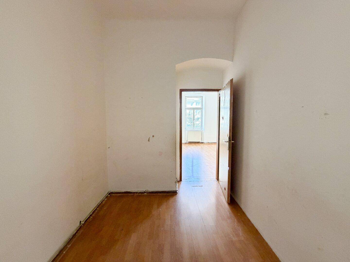 Flur mit Holzboden und offener Tür, die den Blick in einen weiteren Raum freigibt.