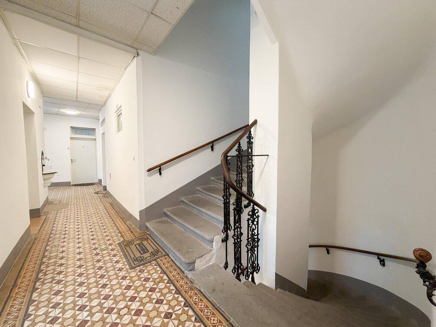 Historisches Treppenhaus in einem Altbau mit kunstvollem Geländer und gemustertem Fliesenboden.