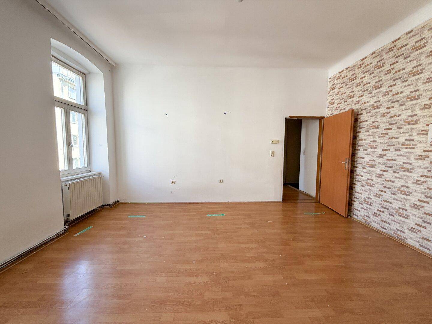 Heller Raum mit Holzboden, einem Fenster und einer dekorativen Tapetenwand.