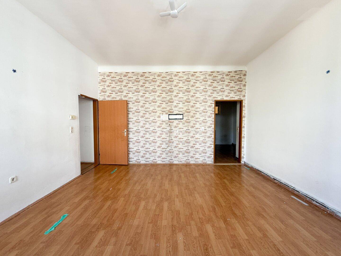 Geräumiges Zimmer mit Holzboden, Deckenventilator und einer Akzentwand mit Tapete.