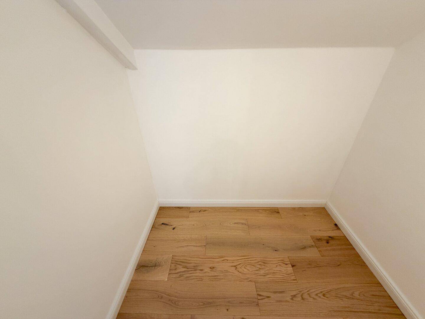 Leerer Abstellraum mit Holzboden und schrägen Wänden, ideal für zusätzlichen Stauraum.