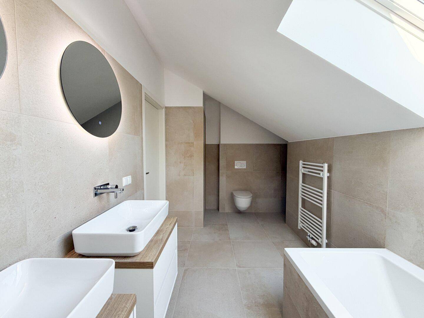 Modernes Badezimmer mit beigefarbenen Fliesen, Doppelwaschbecken, Badewanne und Dachfenster.