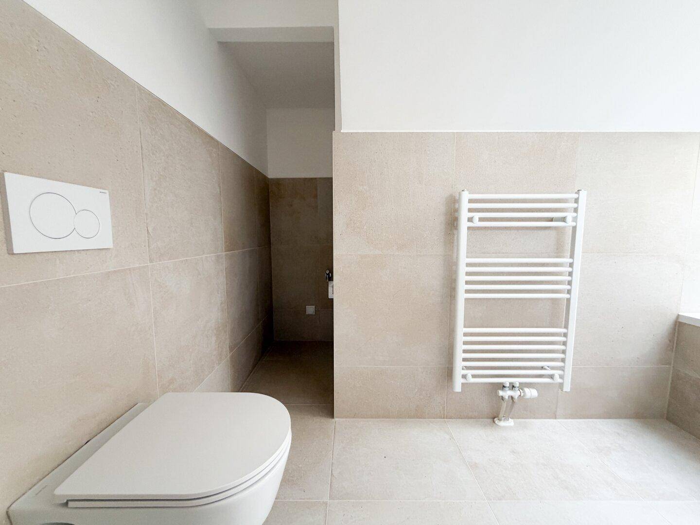 Modernes Badezimmer mit Wand-WC, beigefarbenen Fliesen und beheiztem Handtuchhalter.