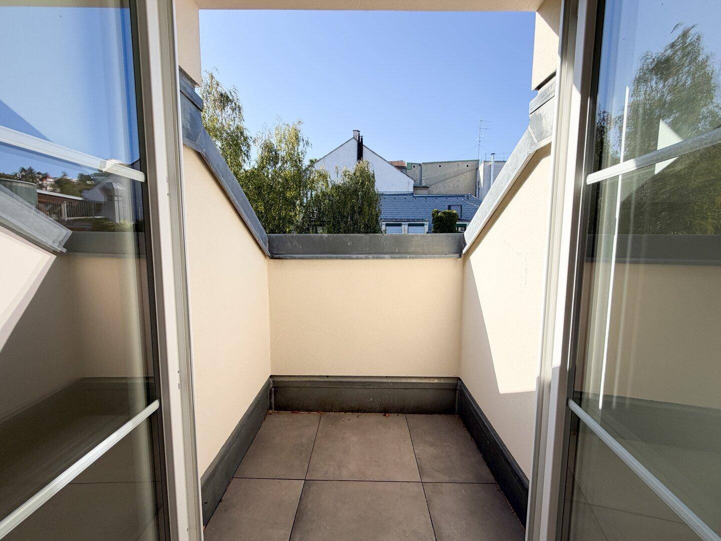 Kleiner, überdachter Balkon mit Fliesenboden und Blick auf die umliegenden Dächer.