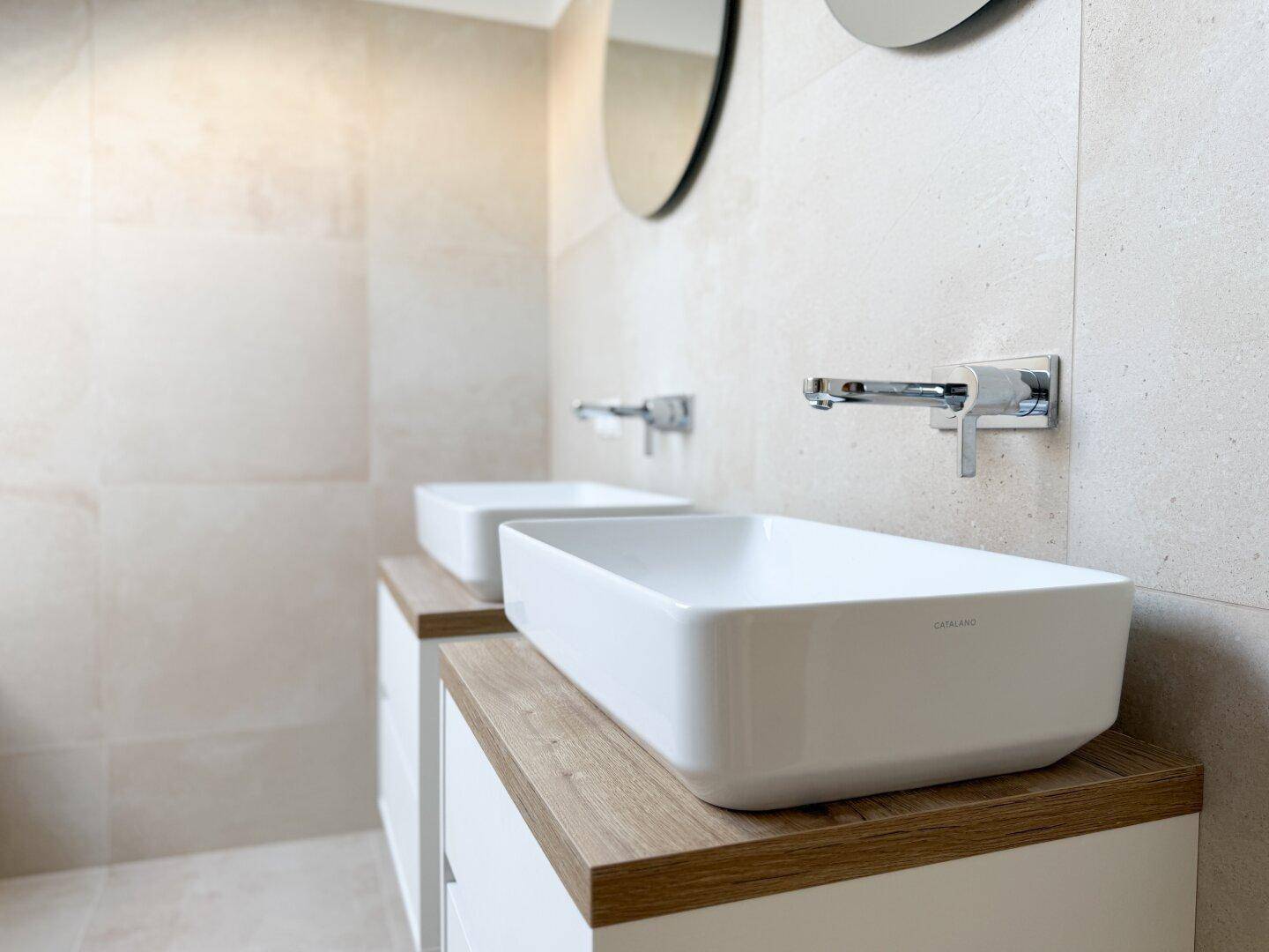 Elegantes Badezimmer mit Doppelwaschbecken, modernen Armaturen und großformatigen Fliesen.