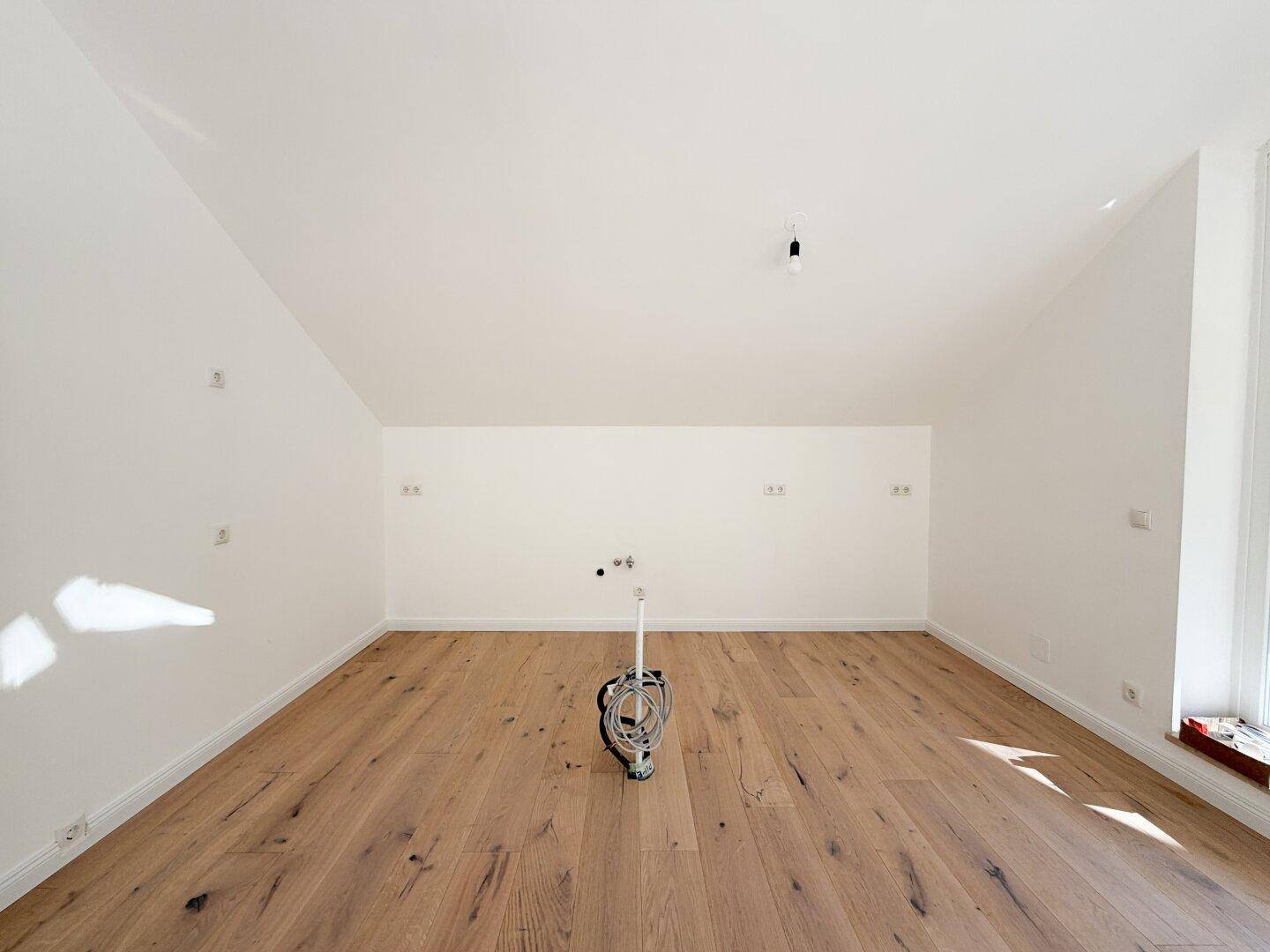 Leerer Raum mit Holzboden und Anschlüssen, ideal für eine offene Küche oder Essbereich.