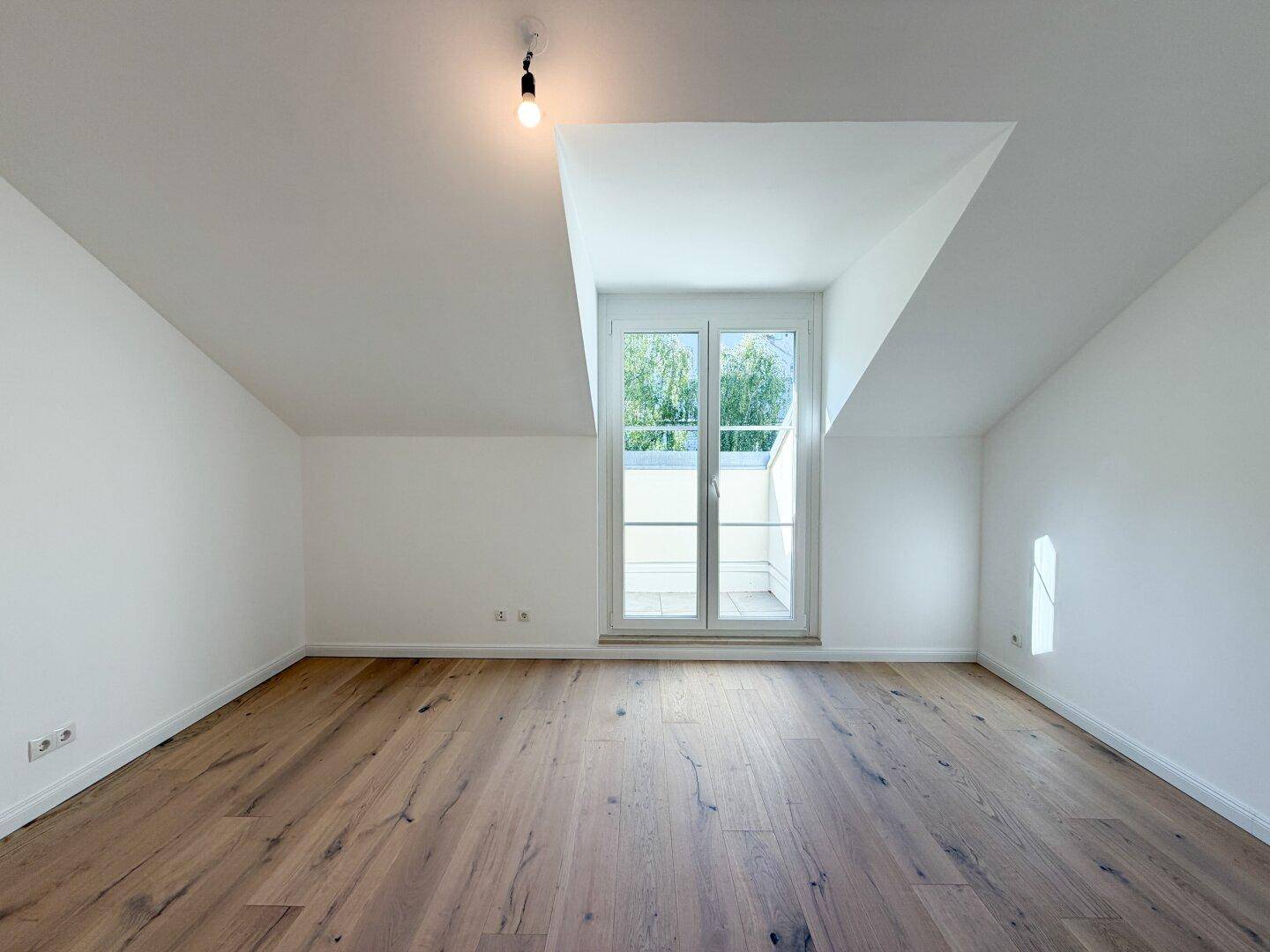 Helles Schlafzimmer mit Holzboden, schrägen Decken und französischem Balkon.