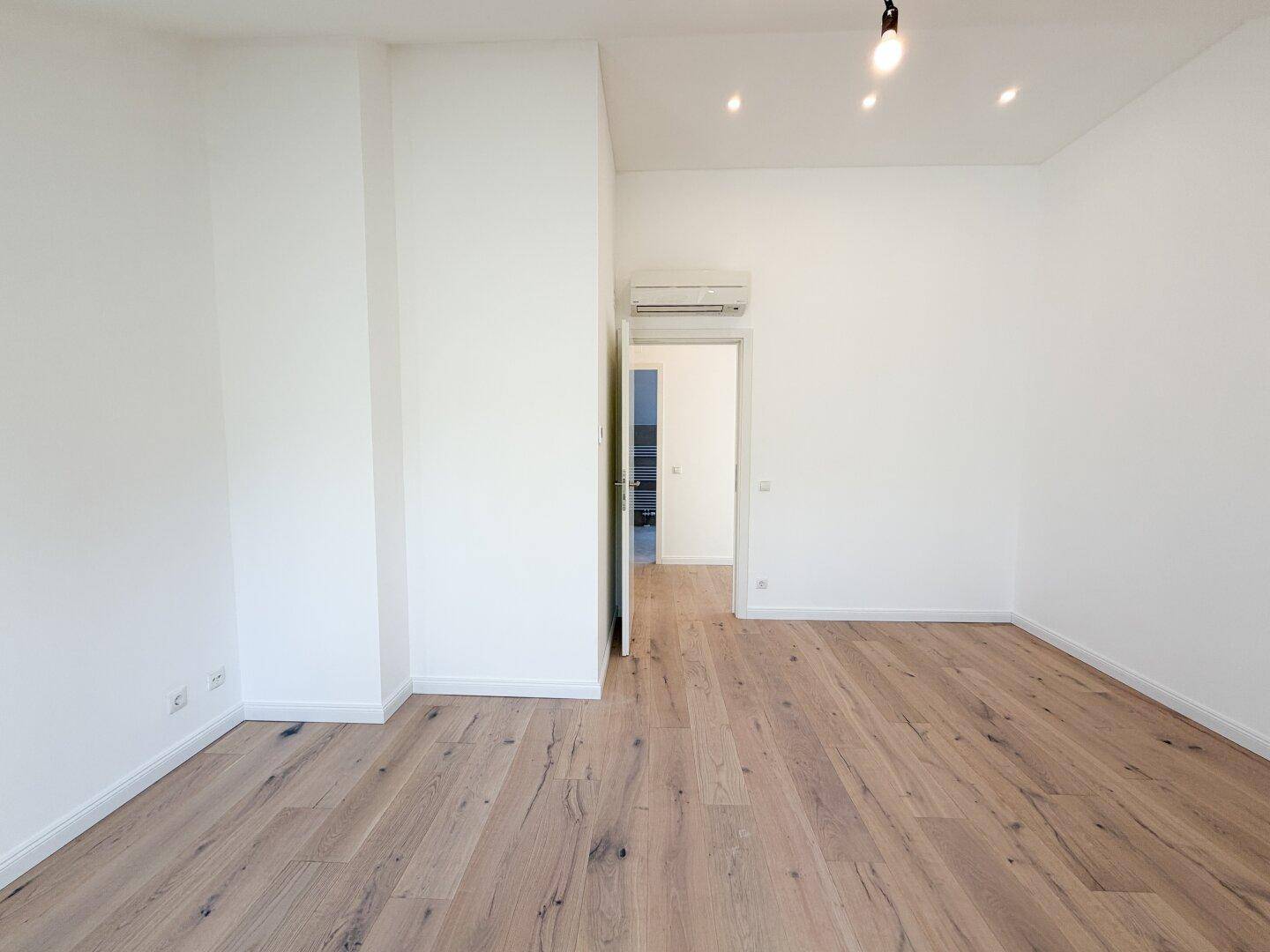 Geräumiges Zimmer mit Holzboden, Klimaanlage und Zugang zu weiteren Räumen.
